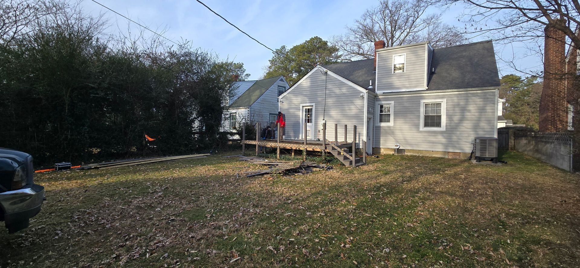 Small white house with enclosed porch and lawn, viewed from the backyard on a sunny autumn day