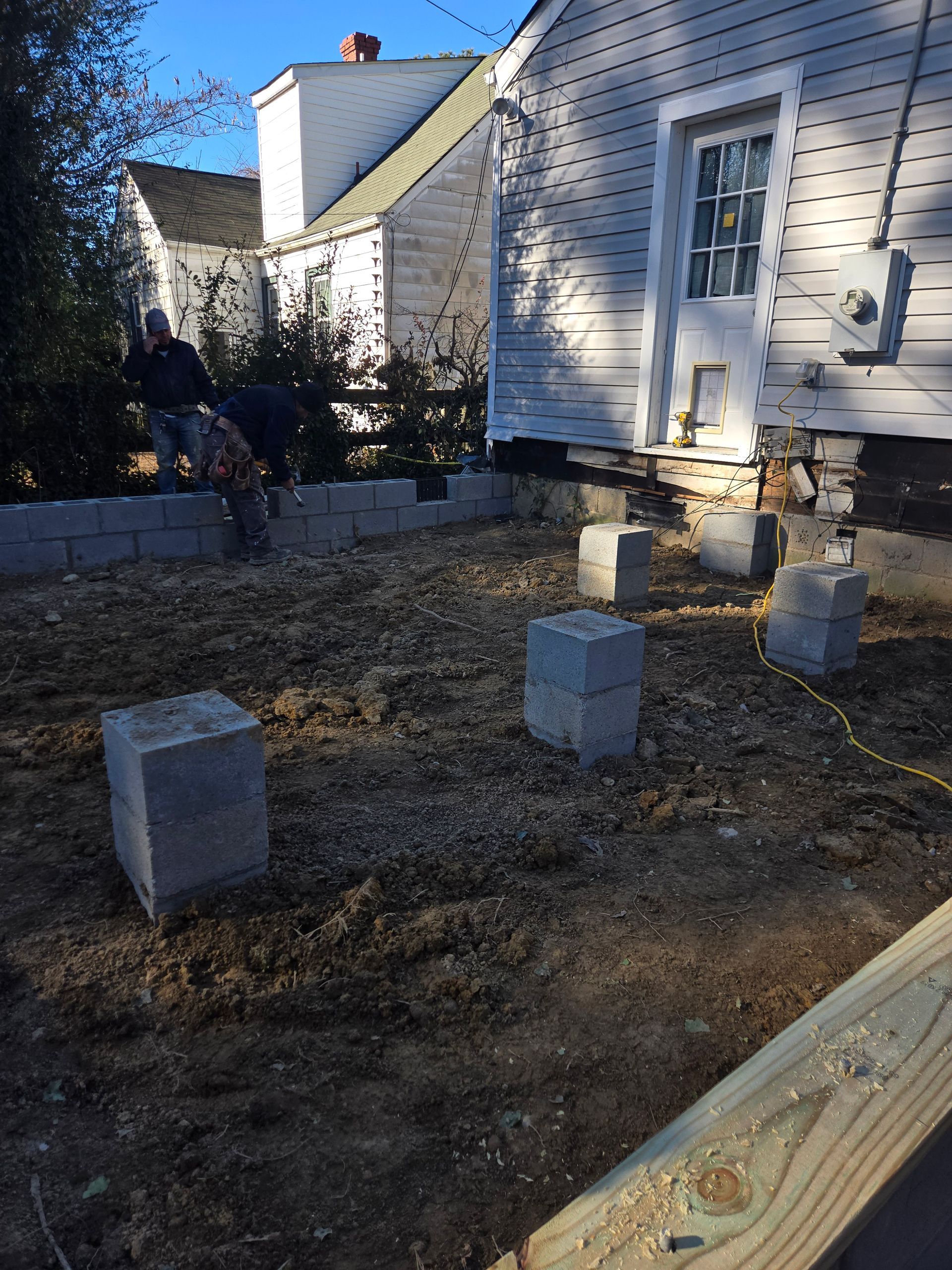 Backyard with a white house, small concrete blocks, and a patchy dirt area under construction
