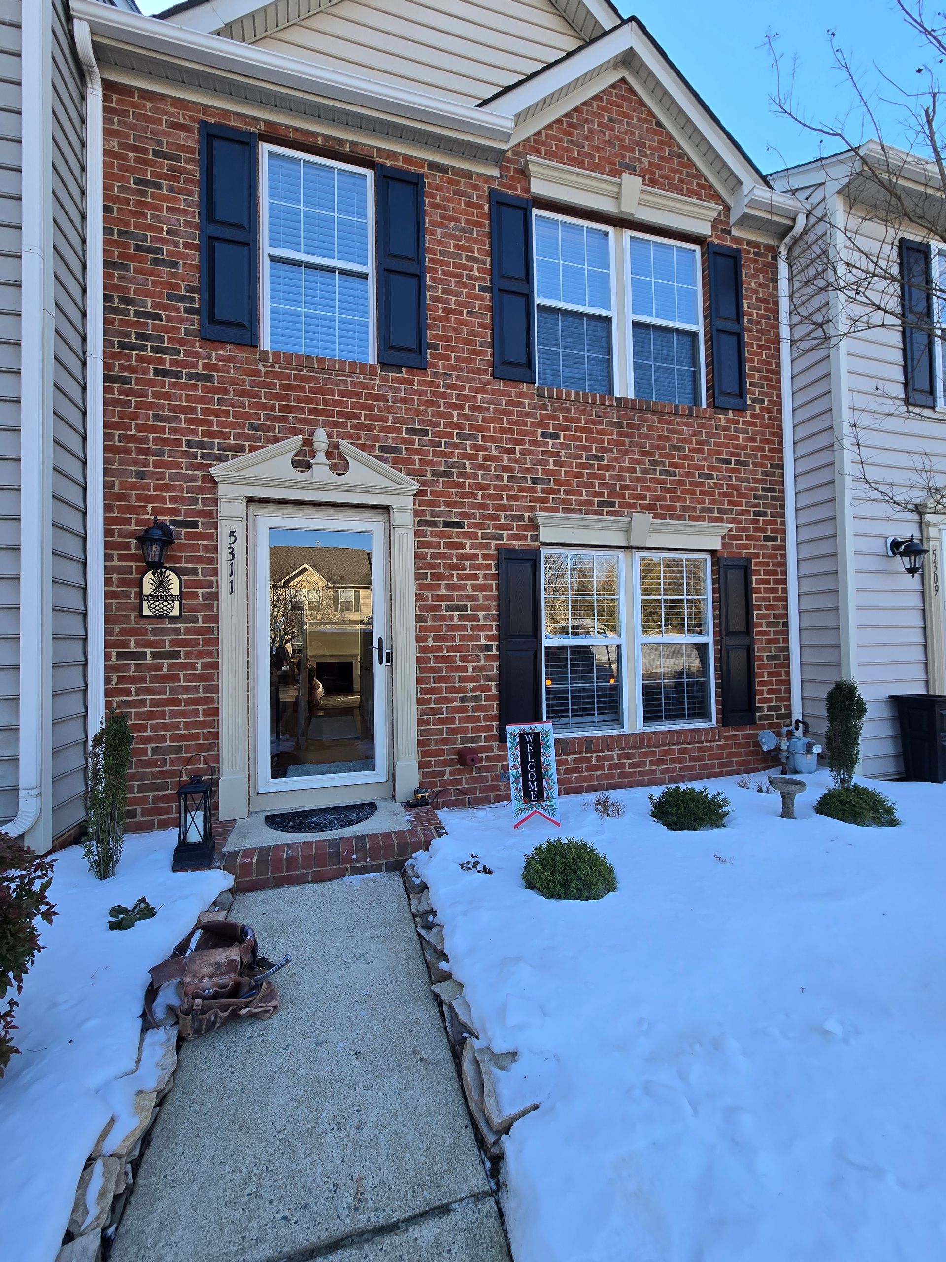 Snow-covered brick townhouse with black shutters and a front walkway