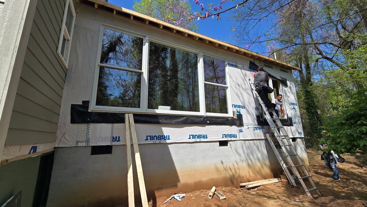 House exterior under renovation with window coverings, ladder, and construction materials outside