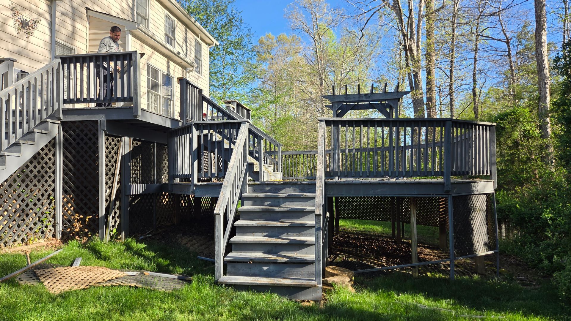 Wooden deck stairs and platforms beside a house, surrounded by trees and green grass.