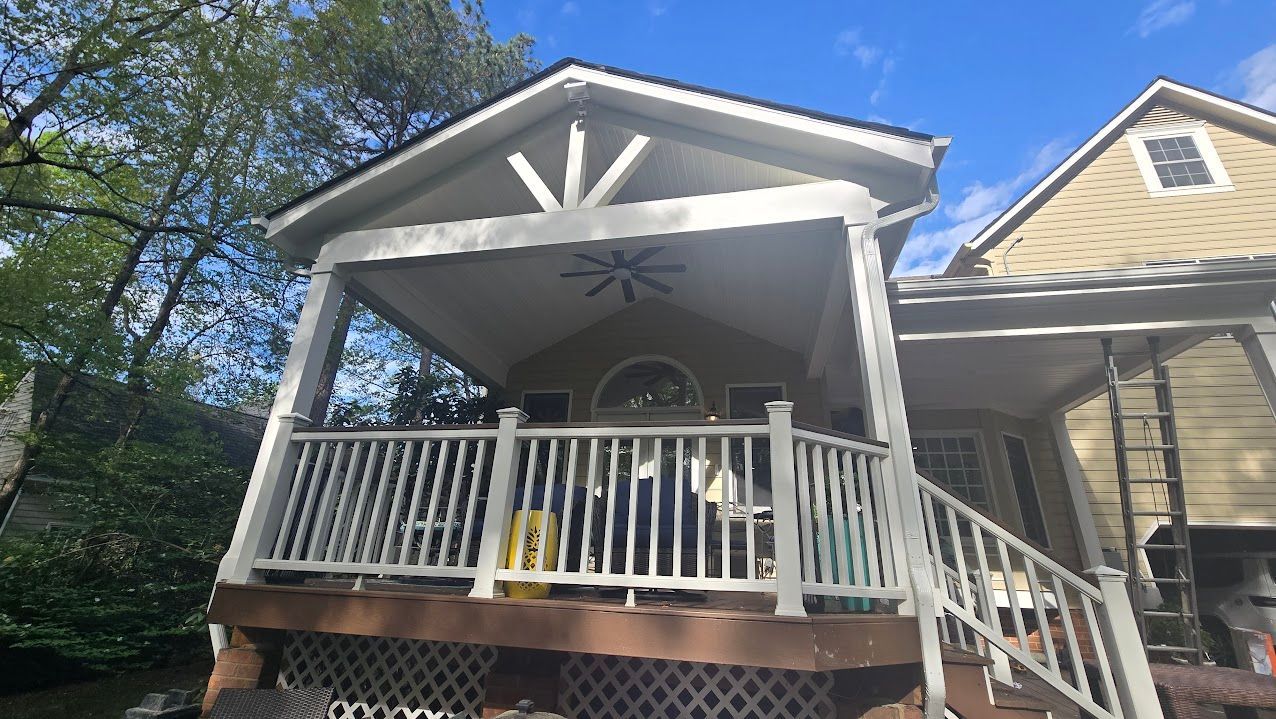 Covered front porch with white railings and a hanging chair on a beige house in daylight