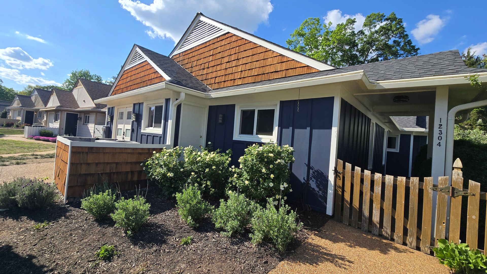 Single-story house with orange-tiled roof, white trim, dark windows, and a small front garden under a blue sky