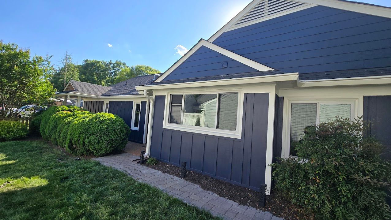 Blue house exterior with white trim, front window, and green shrubs along a sunny walkway