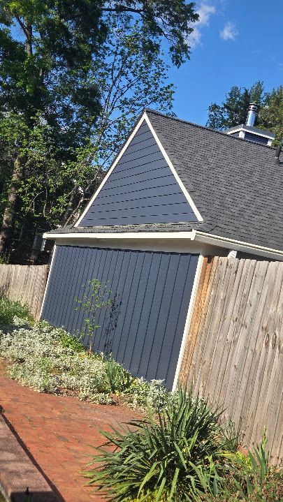 Blue-roofed garage beside a wooden fence, with red paving and garden plants under a sunny sky