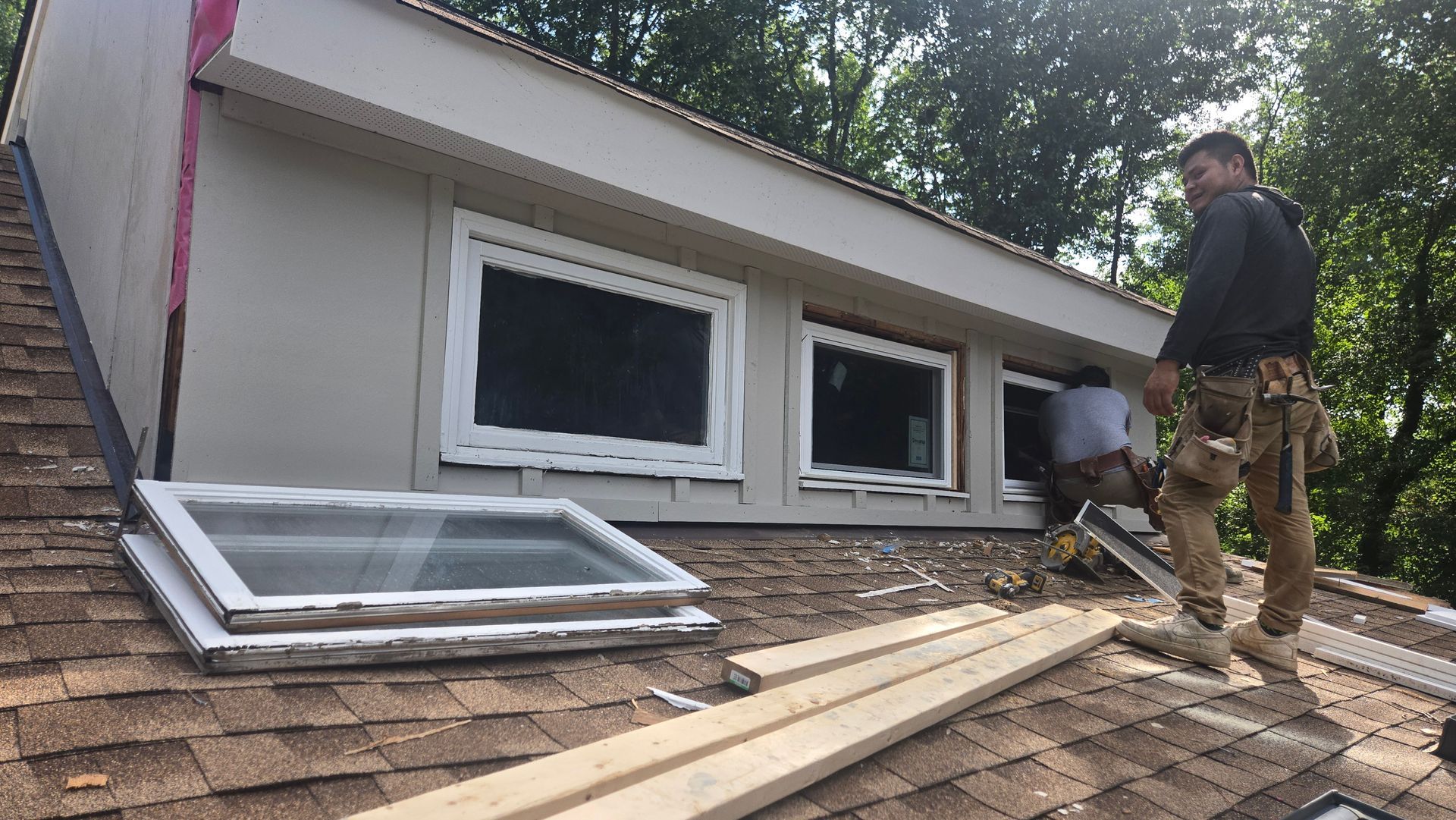 Workers repairing a roof around two white-framed windows on a house