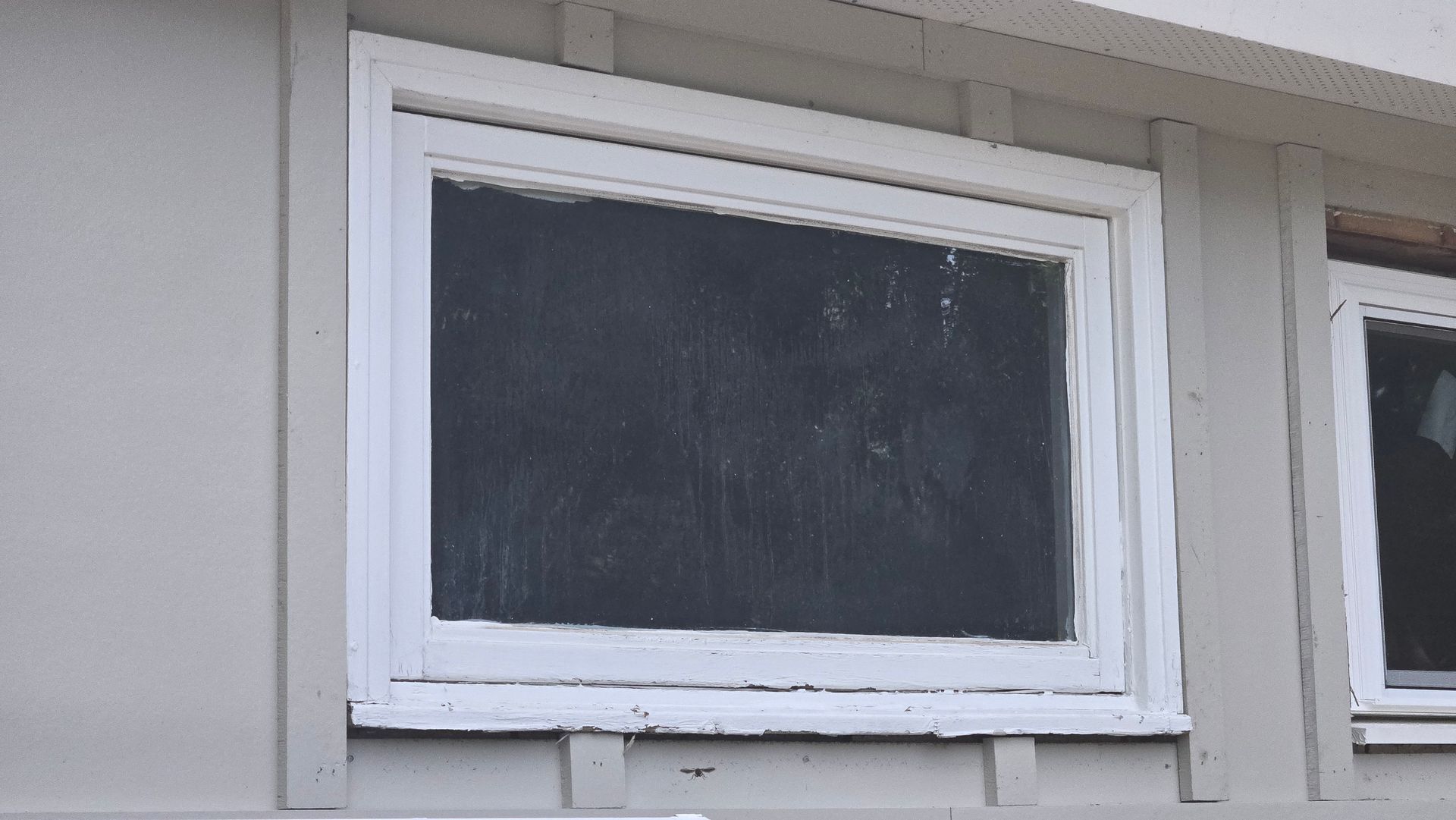 White-framed window with a dark screen on a light gray building exterior