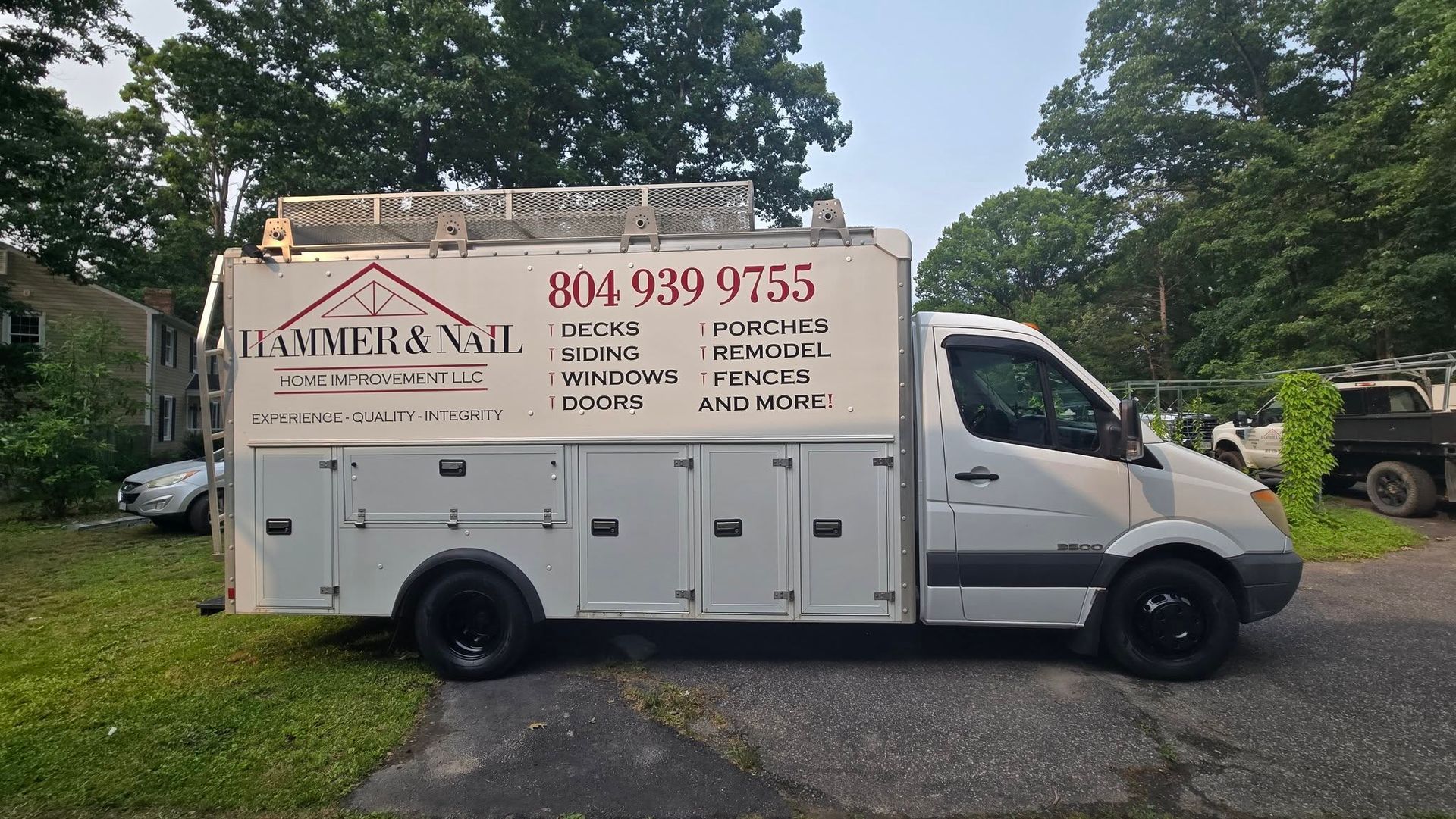 White service van with business signage parked on a driveway by trees and grass