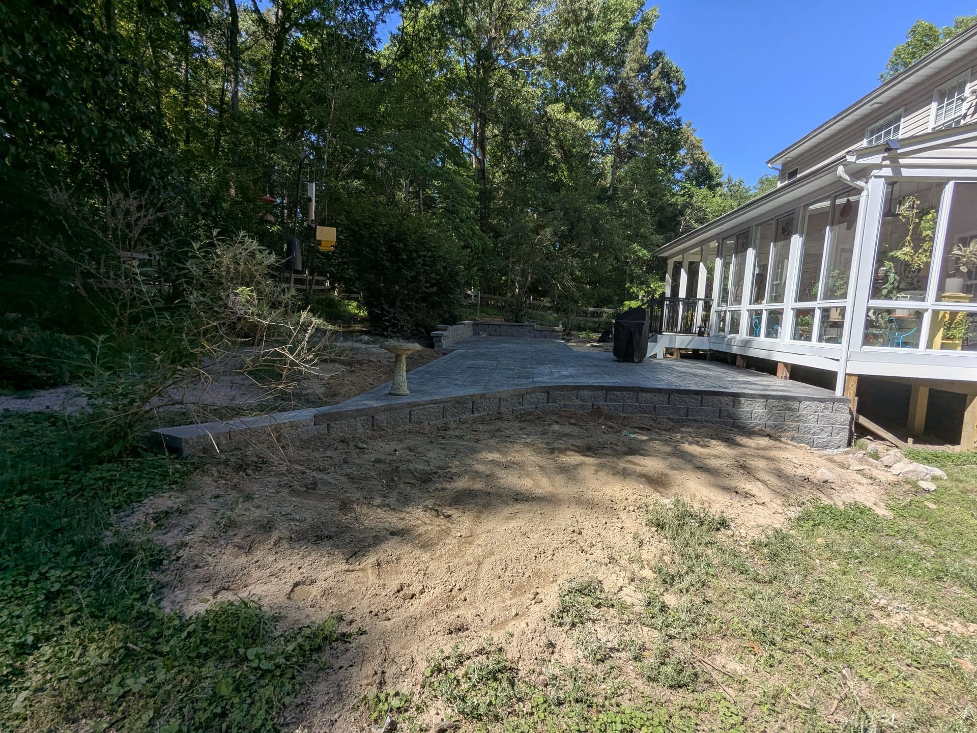 Dry dirt yard beside a white screened porch, with trees and a curved gravel path leading into the woods
