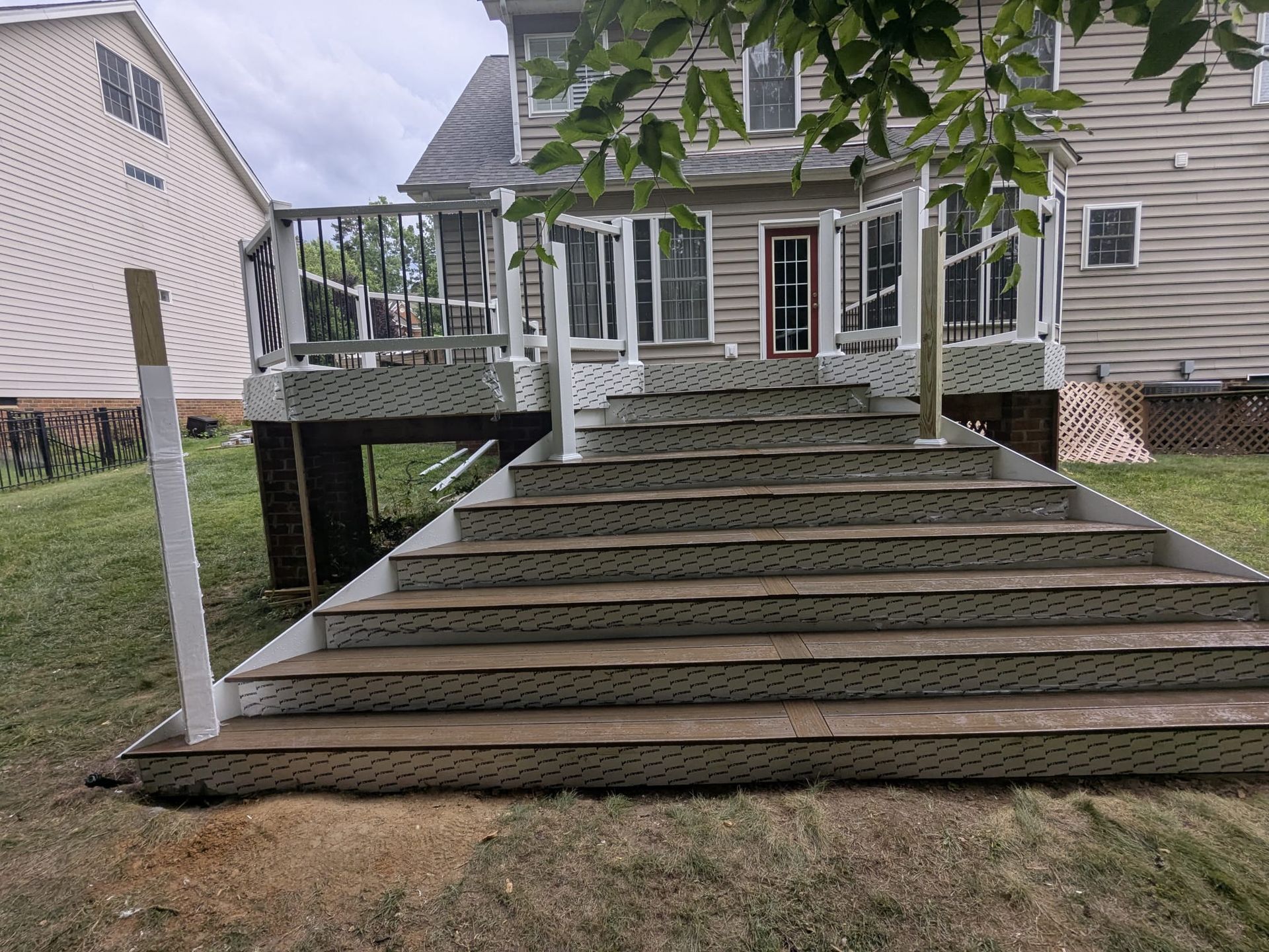 Backyard deck with wide wooden stairs leading to a white house porch