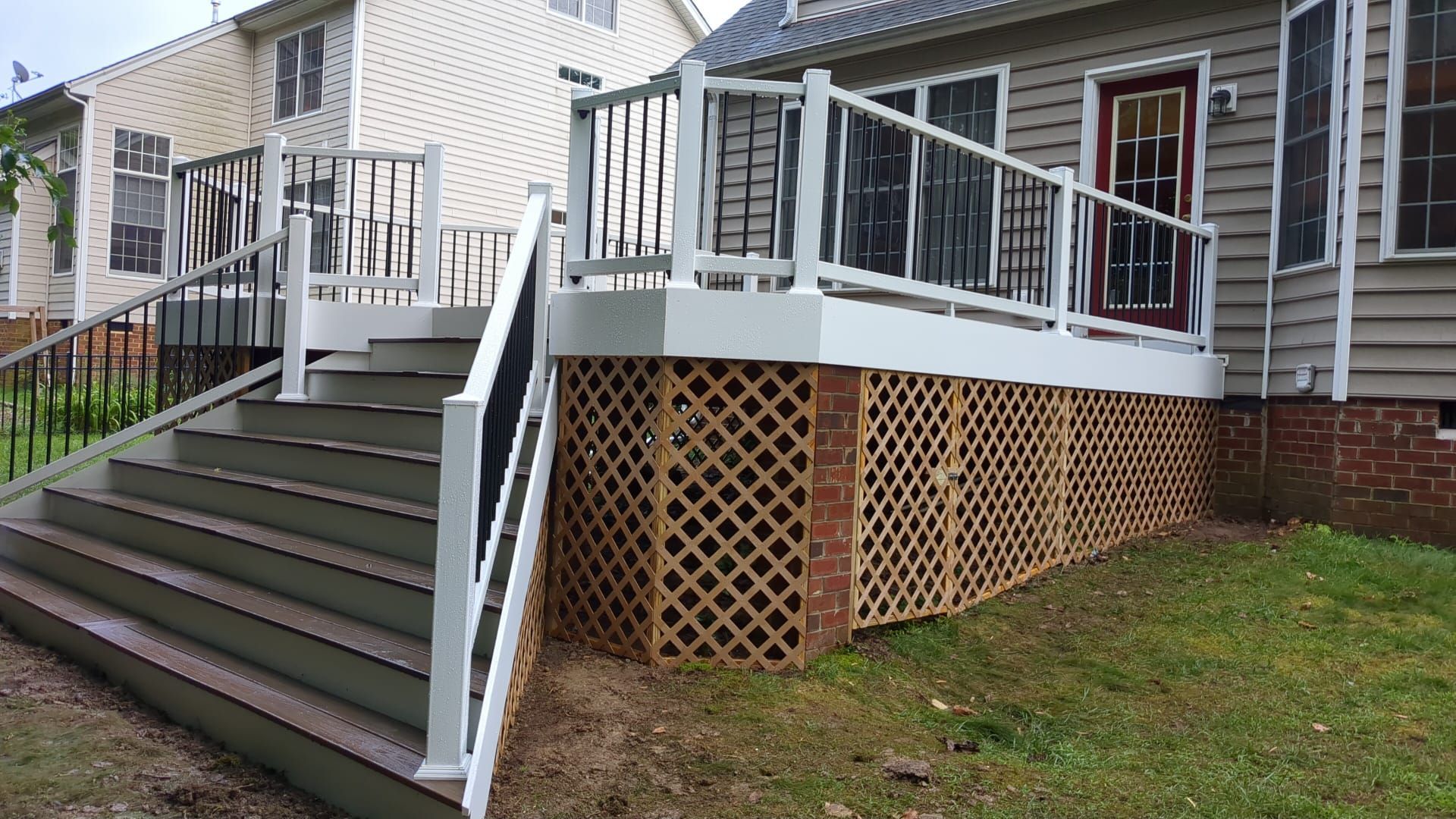 Stairway and white-railed deck on the side of a gray house with lattice skirting and grass below