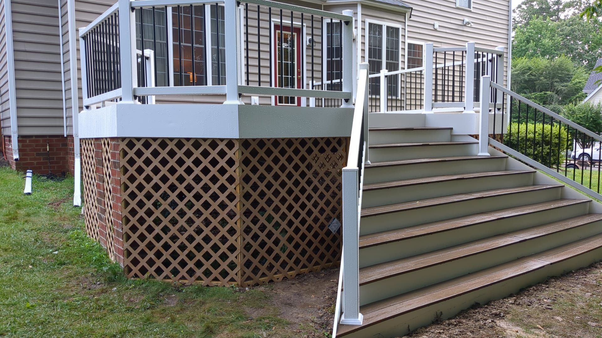House porch with white railings, lattice skirting, and wide wooden steps leading to a side entrance.