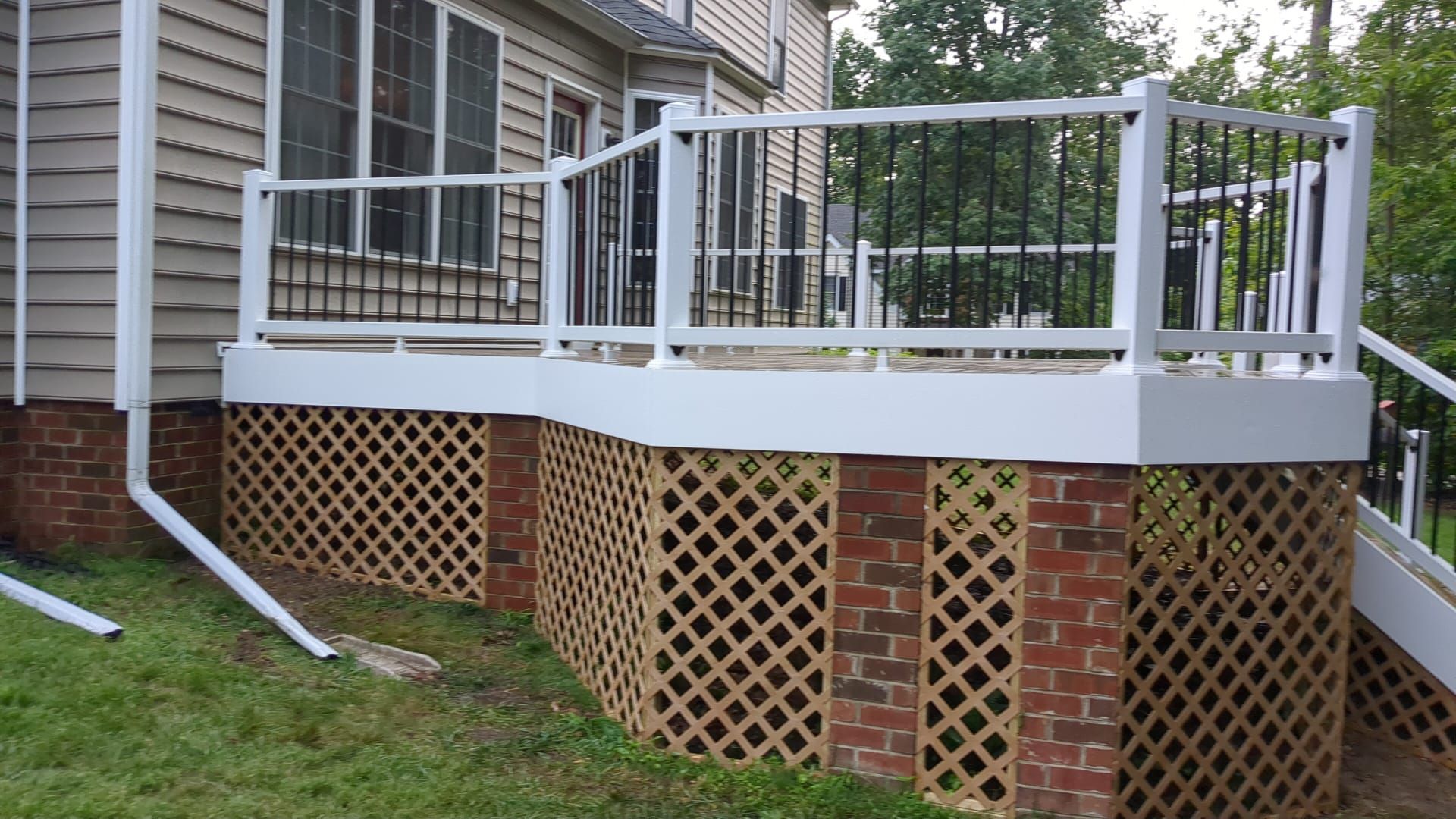 Elevated white deck with metal railing attached to a house, with brick lattice skirting and stairs nearby