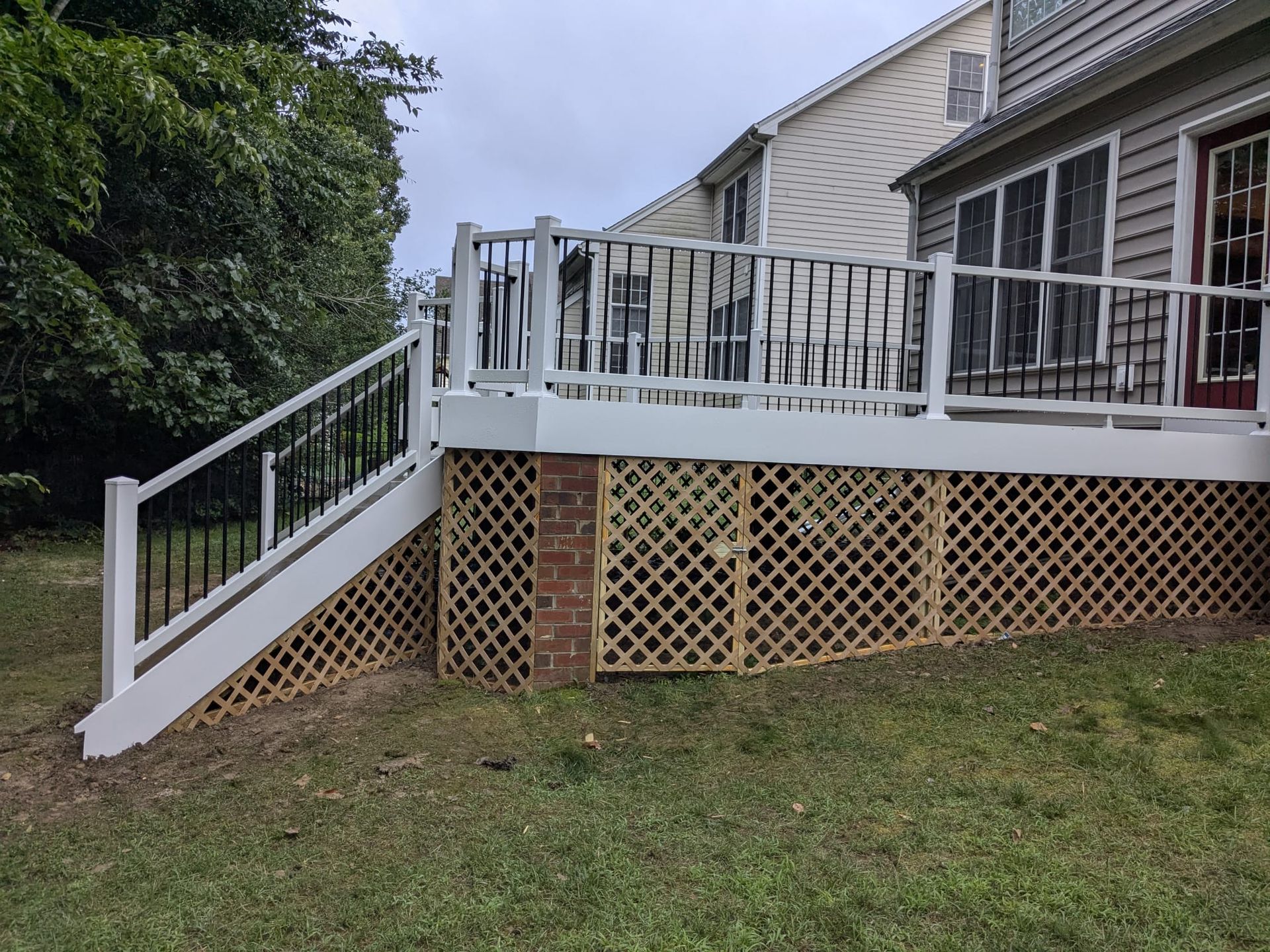 White-railed deck with stairs and lattice skirting on a house beside a grassy yard.