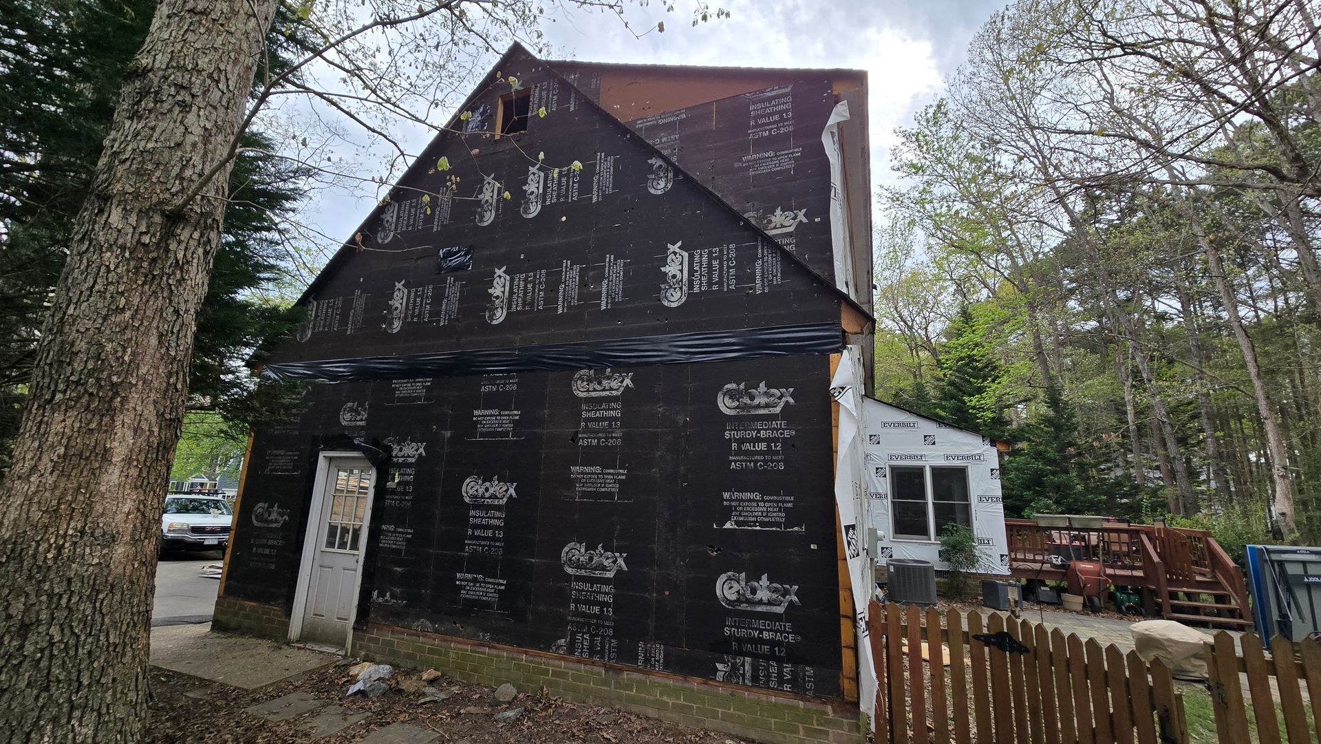 House under renovation with dark wrap, white siding, and wooded yard