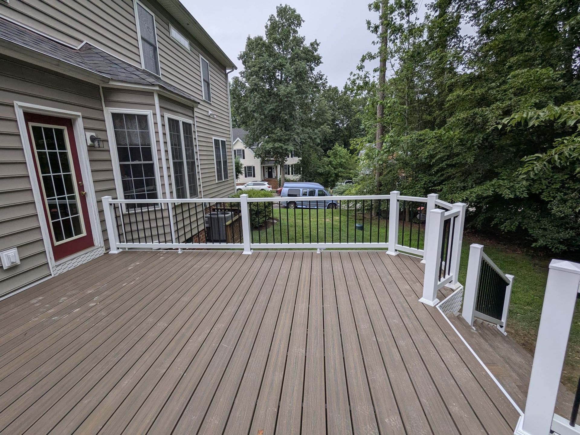 Wooden backyard deck beside a house, with white railings and a wooded yard beyond.