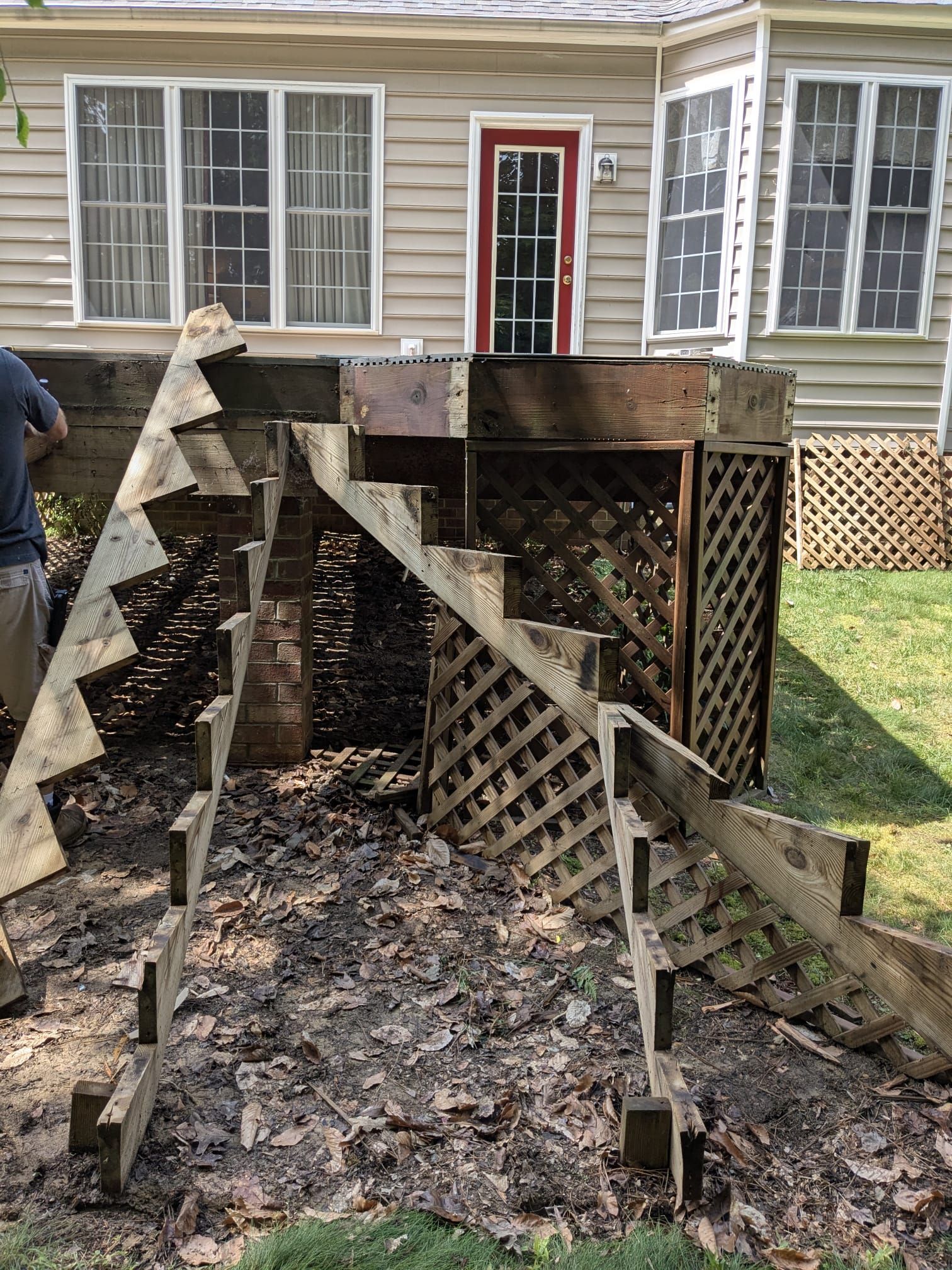 Collapsed wooden deck ramp in a backyard, with broken supports and a house in the background