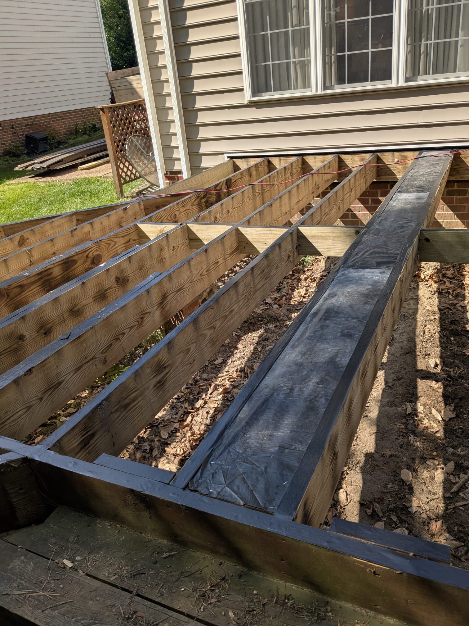 Partially built wooden deck frame beside a beige house with joists and beams exposed
