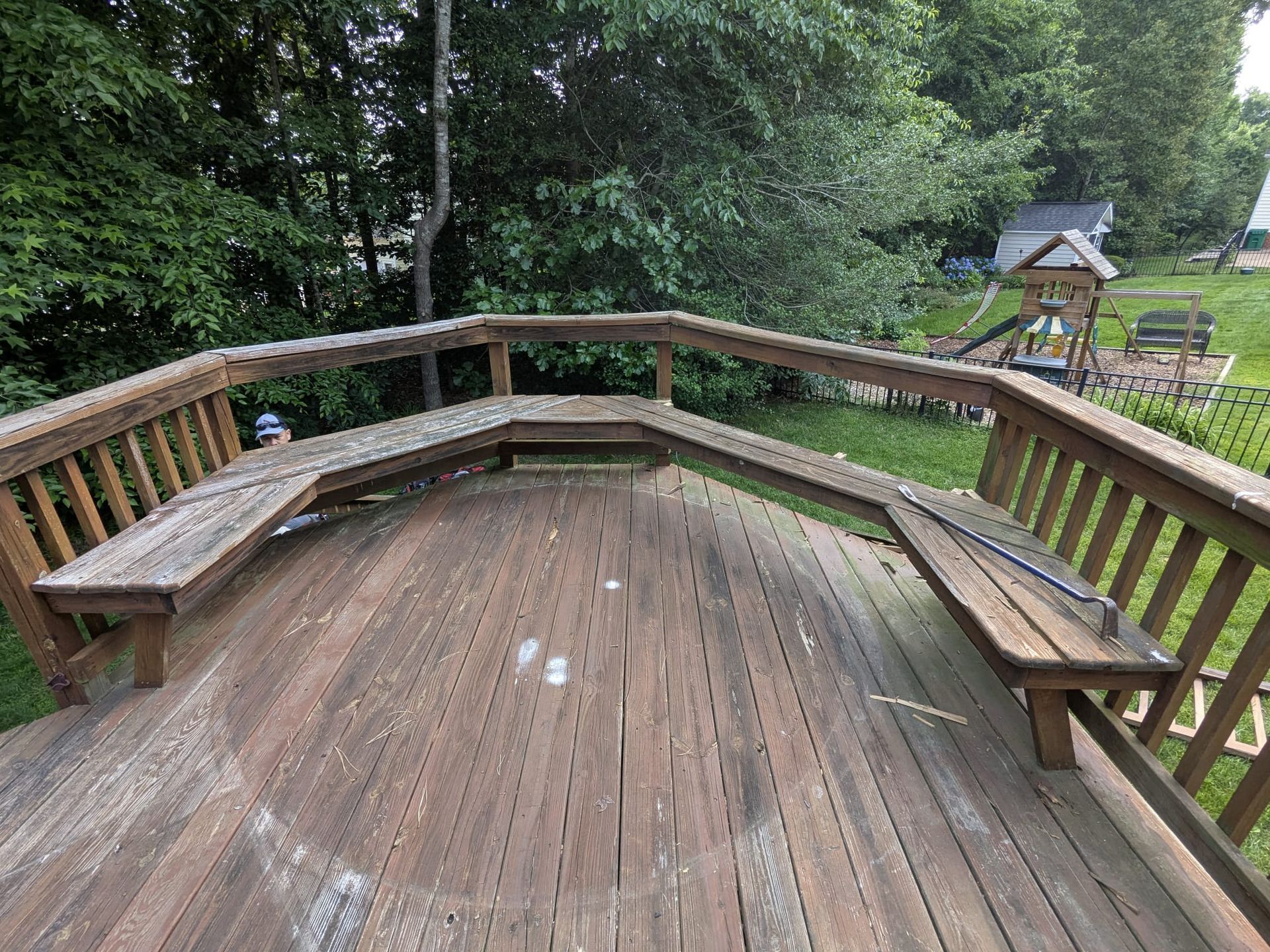 Curved wooden deck with benches overlooking a grassy backyard and trees