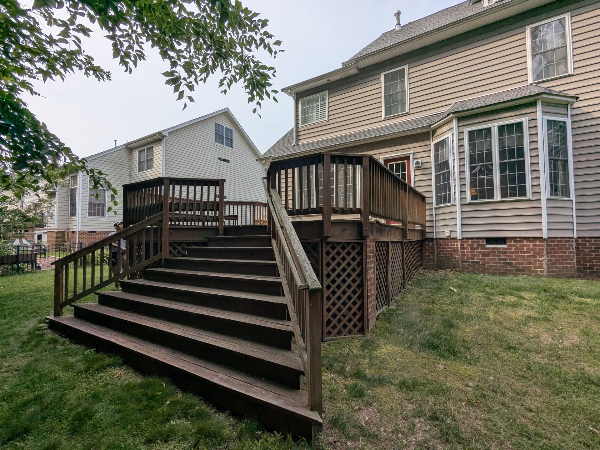 Wooden deck stairs leading to a house with a raised porch and white-sided outbuilding