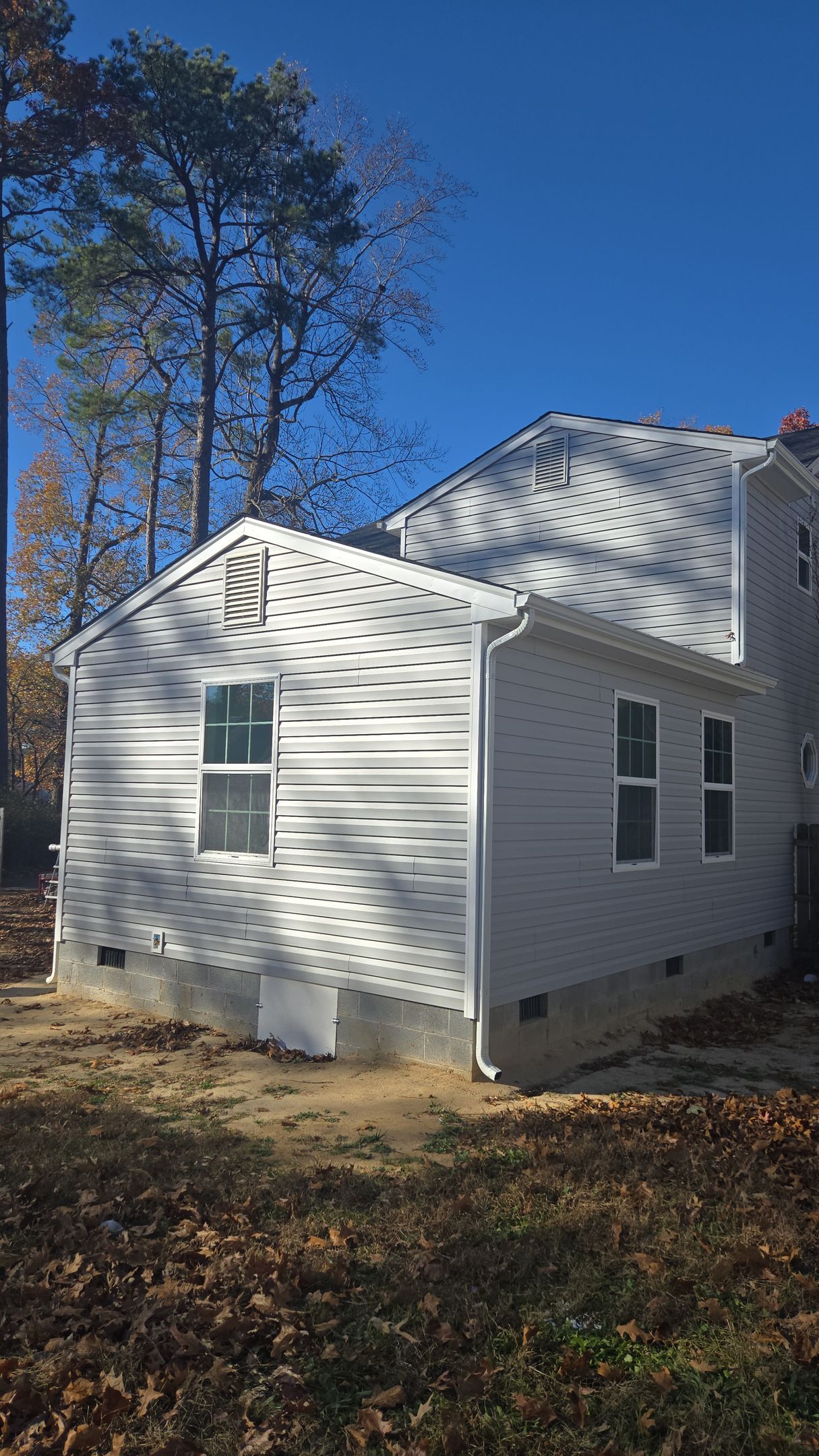 White house with a sloped roof and dormer windows, surrounded by trees in a wooded yard.