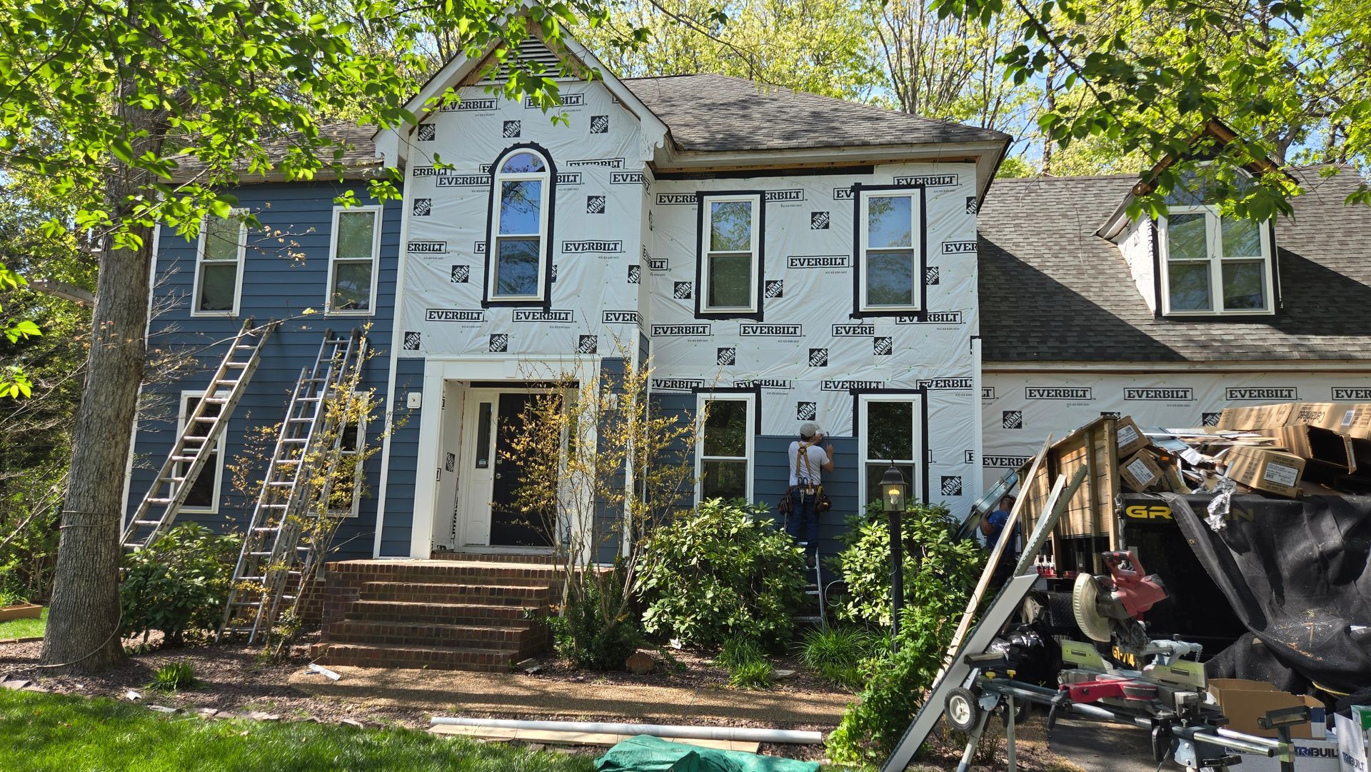 House exterior under renovation with scaffolding, ladders, and debris in the yard.