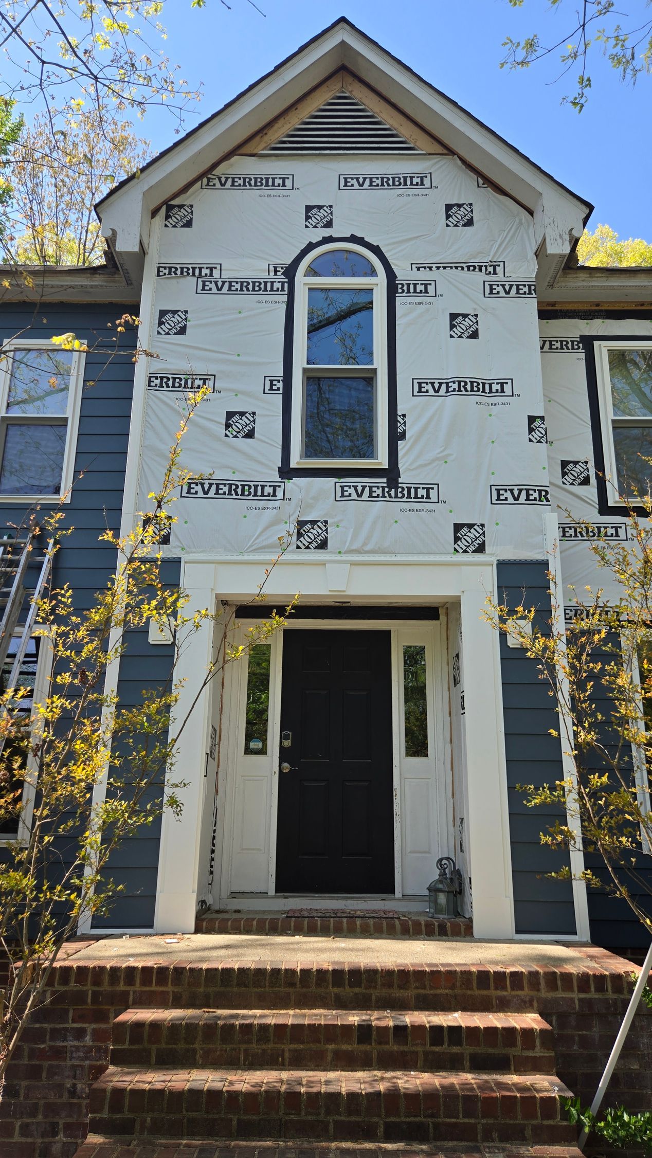 Two-story house under construction with white house wrap, arched window, and front steps.