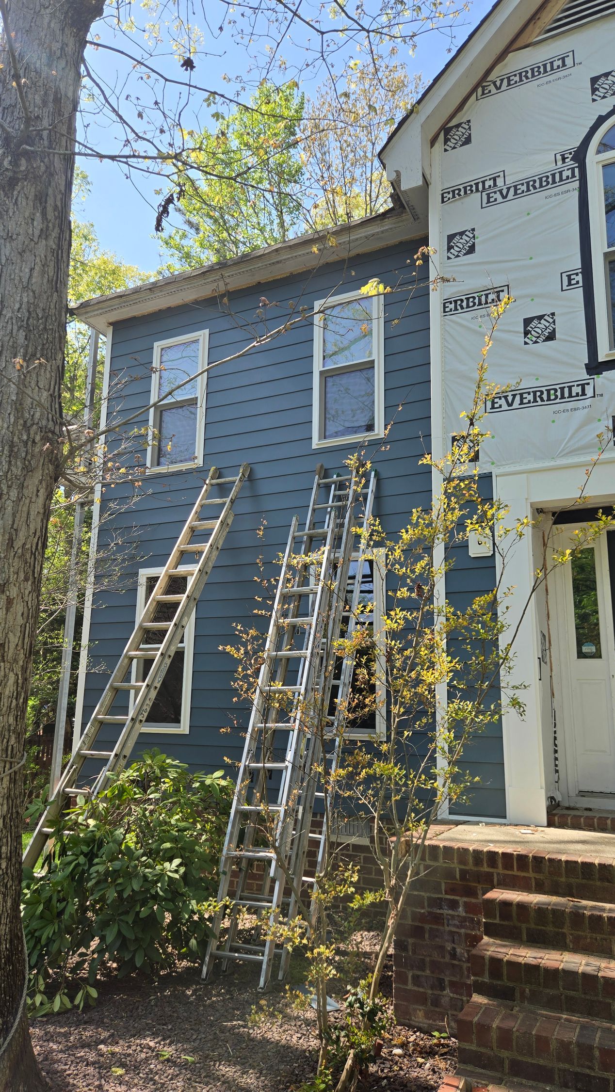 Blue two-story house with white siding, ladders leaning against it, and brick steps in front