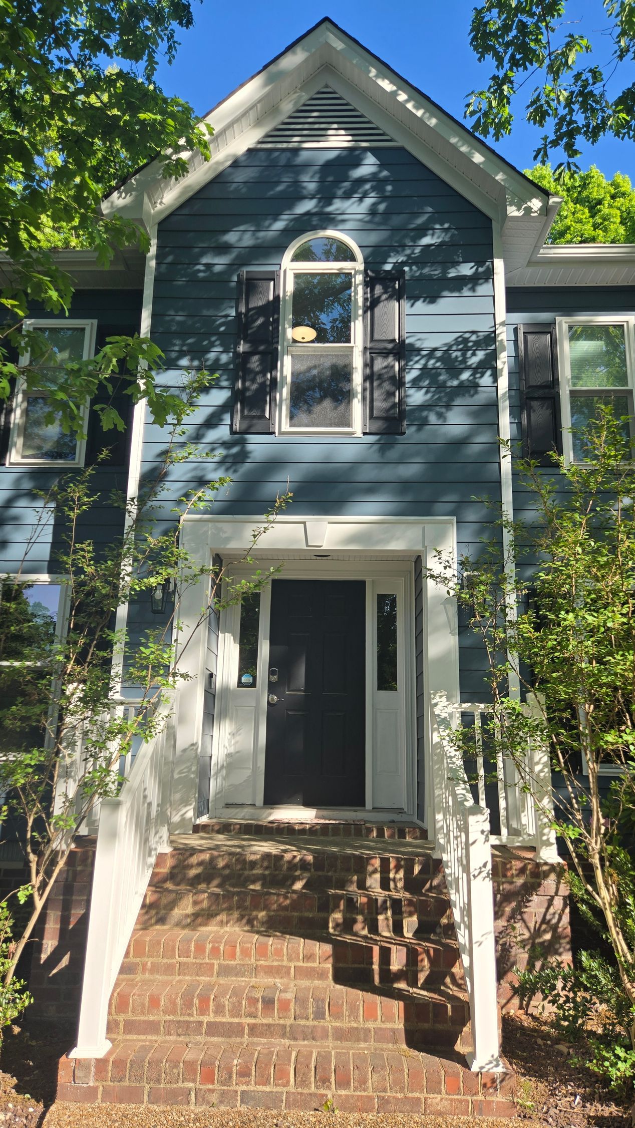 Gray house with white trim and a brick staircase leading to a front porch under trees