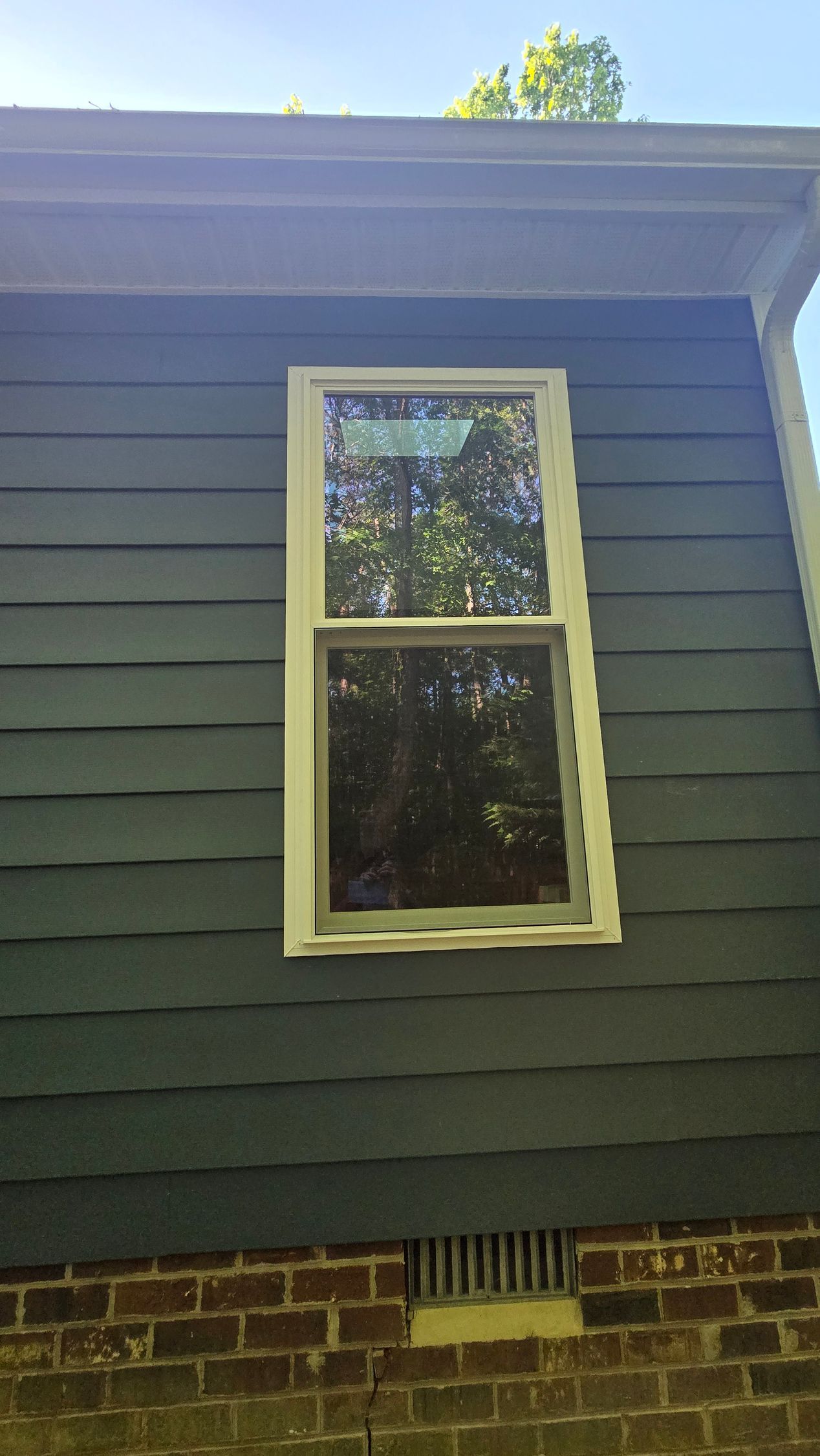 Single white-trimmed window on a dark green house exterior above a brick foundation