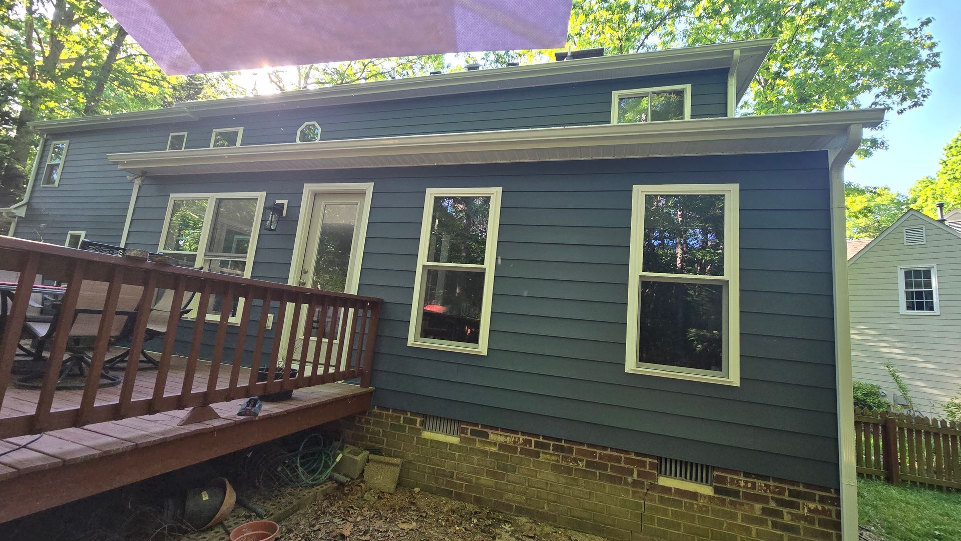 Gray house exterior with porch railing and red-trimmed windows under trees