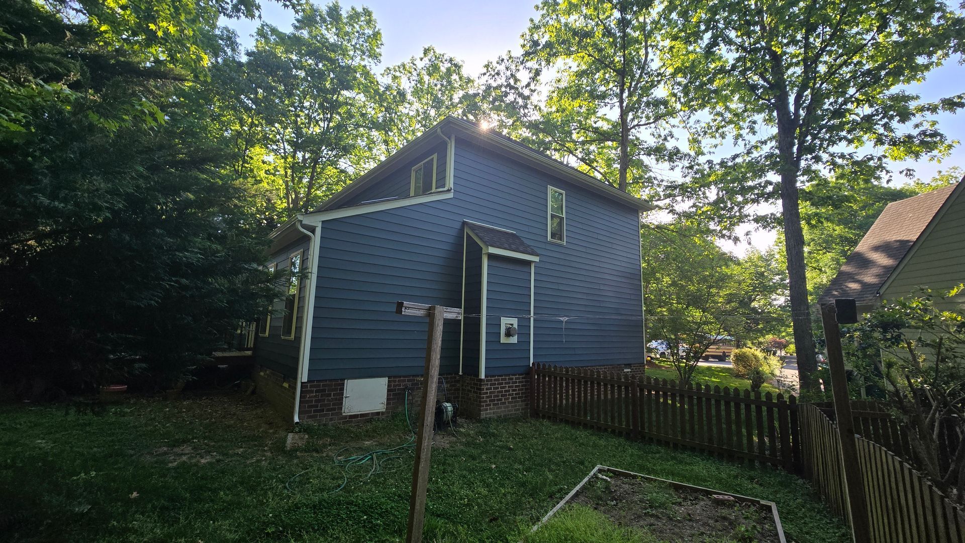 Blue house with a fenced yard and trees in a wooded residential area.