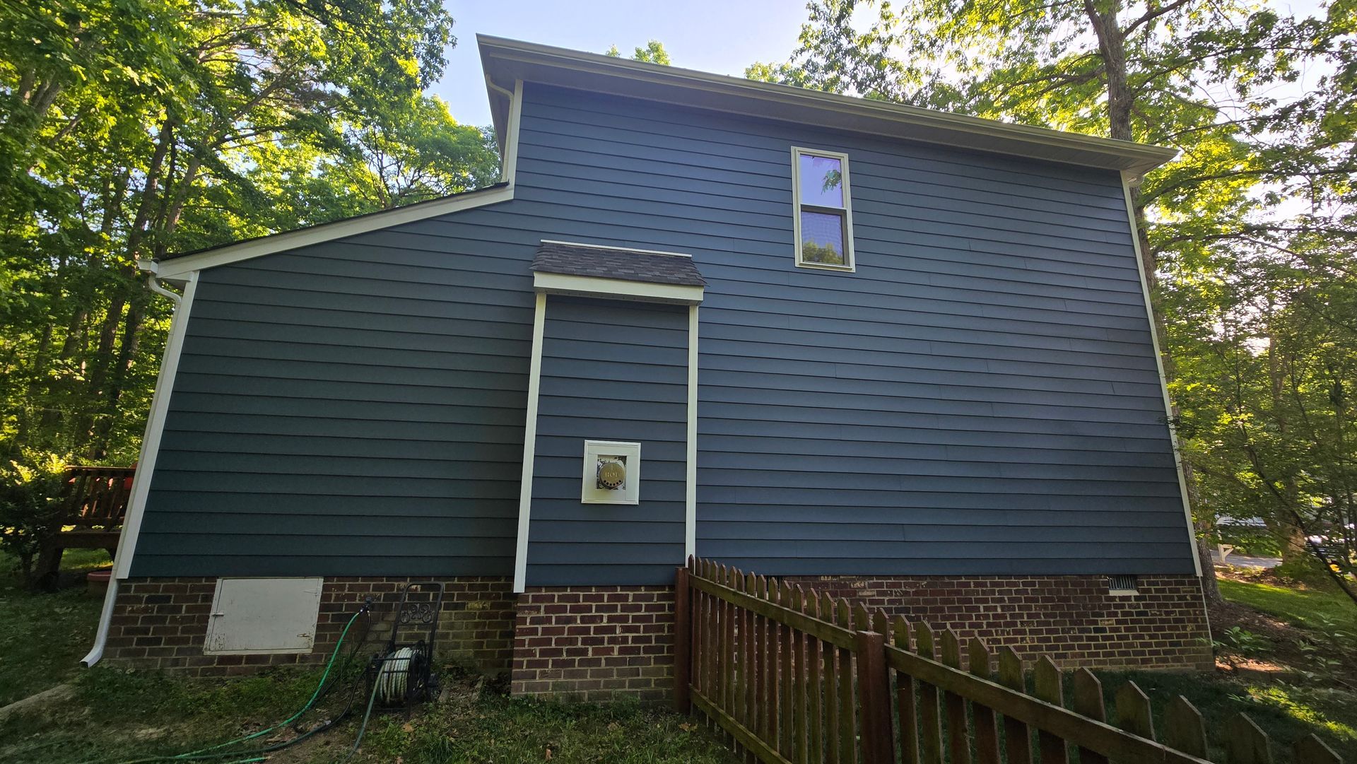 Blue house exterior with brick foundation, small front door, and trees surrounding it