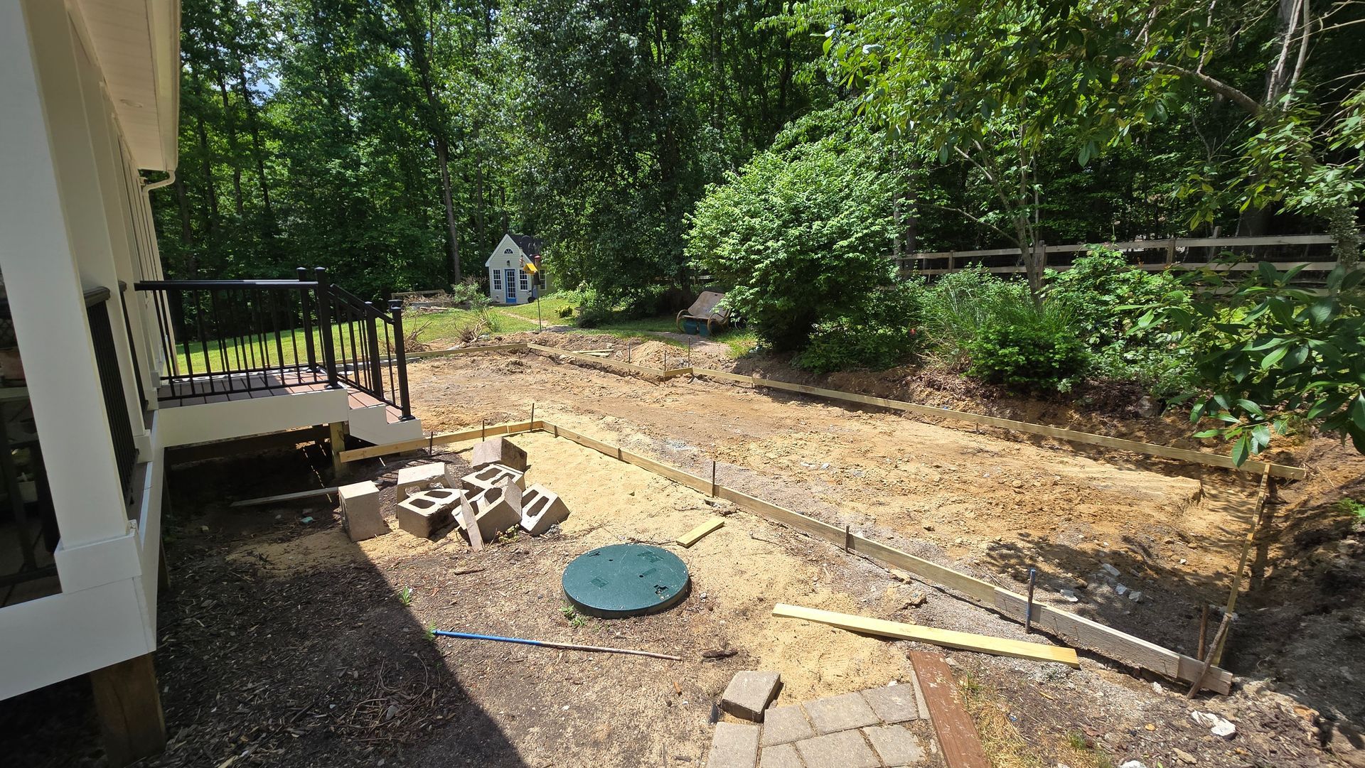 Backyard patio with a brick path, raised garden bed, scattered tools, and trees in bright sun