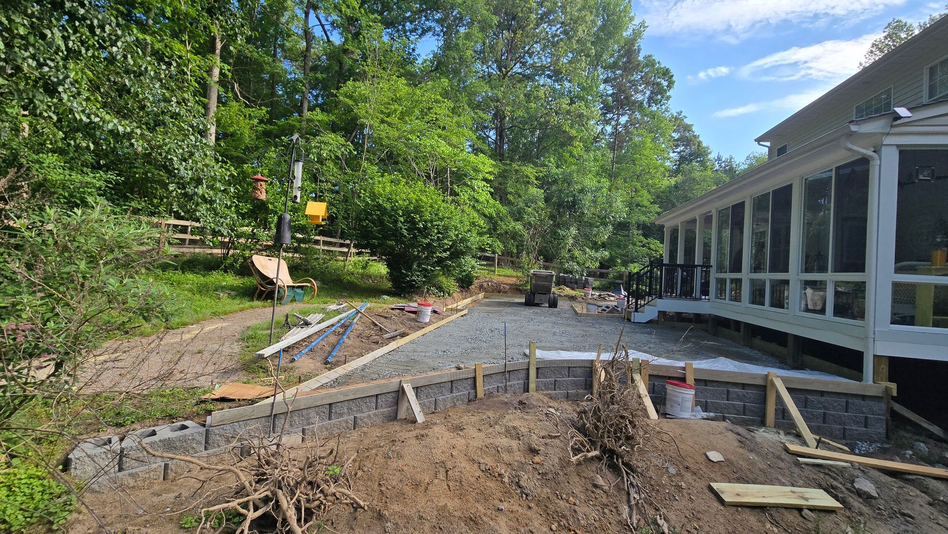 Backyard construction site with gravel, lumber, and a screened porch beside trees