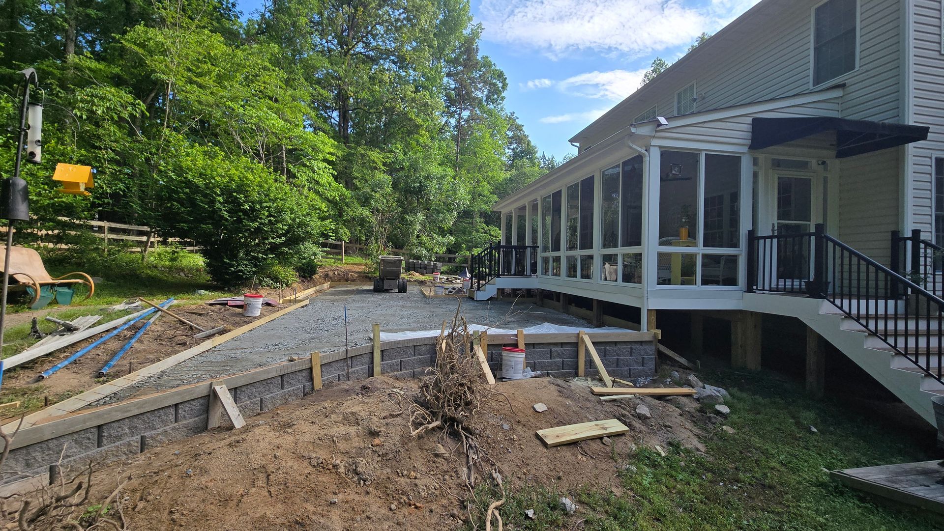 Backyard construction site with concrete forms, dirt piles, and a screened porch on the right.