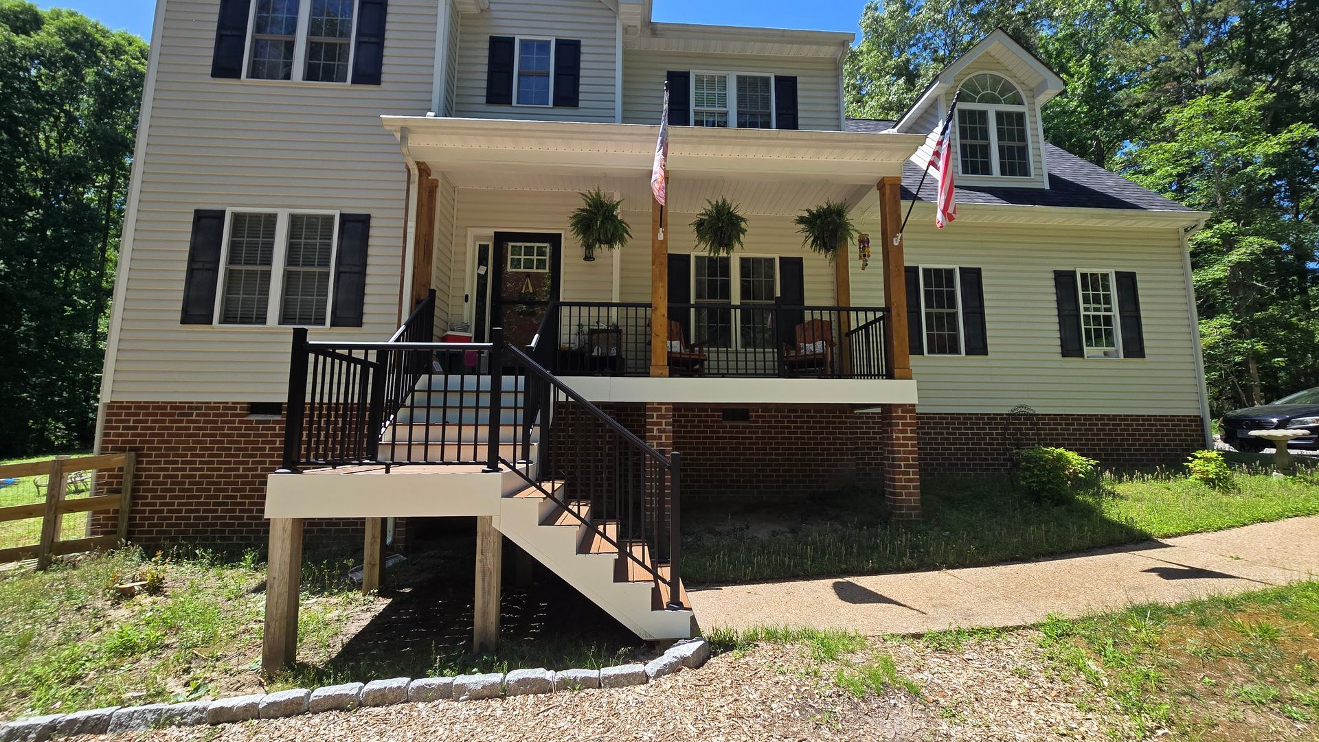 Two-story beige house with black shutters, front porch, and ramp, seen on a sunny day