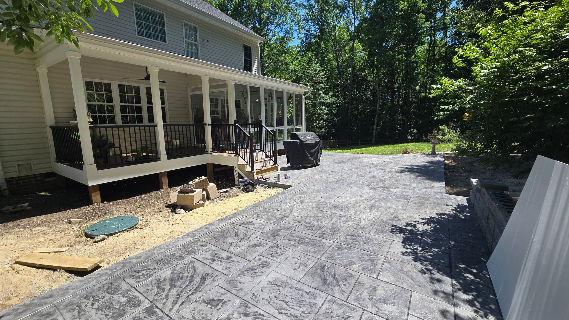 Backyard with a house porch and a newly installed gravel driveway beside a tree-lined yard