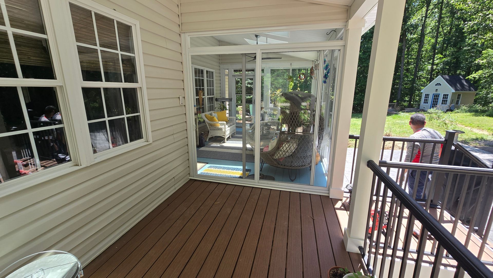 Covered wooden porch with white siding, railing, and sliding glass doors overlooking a backyard.