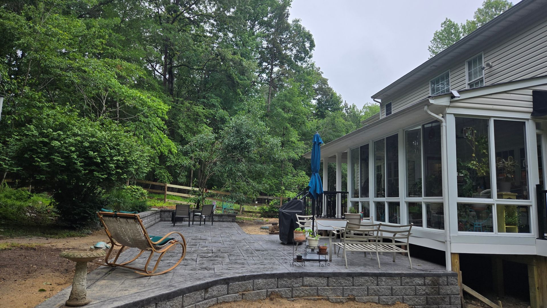 Backyard patio with chairs, fire pit, and screened porch beside a house under cloudy skies