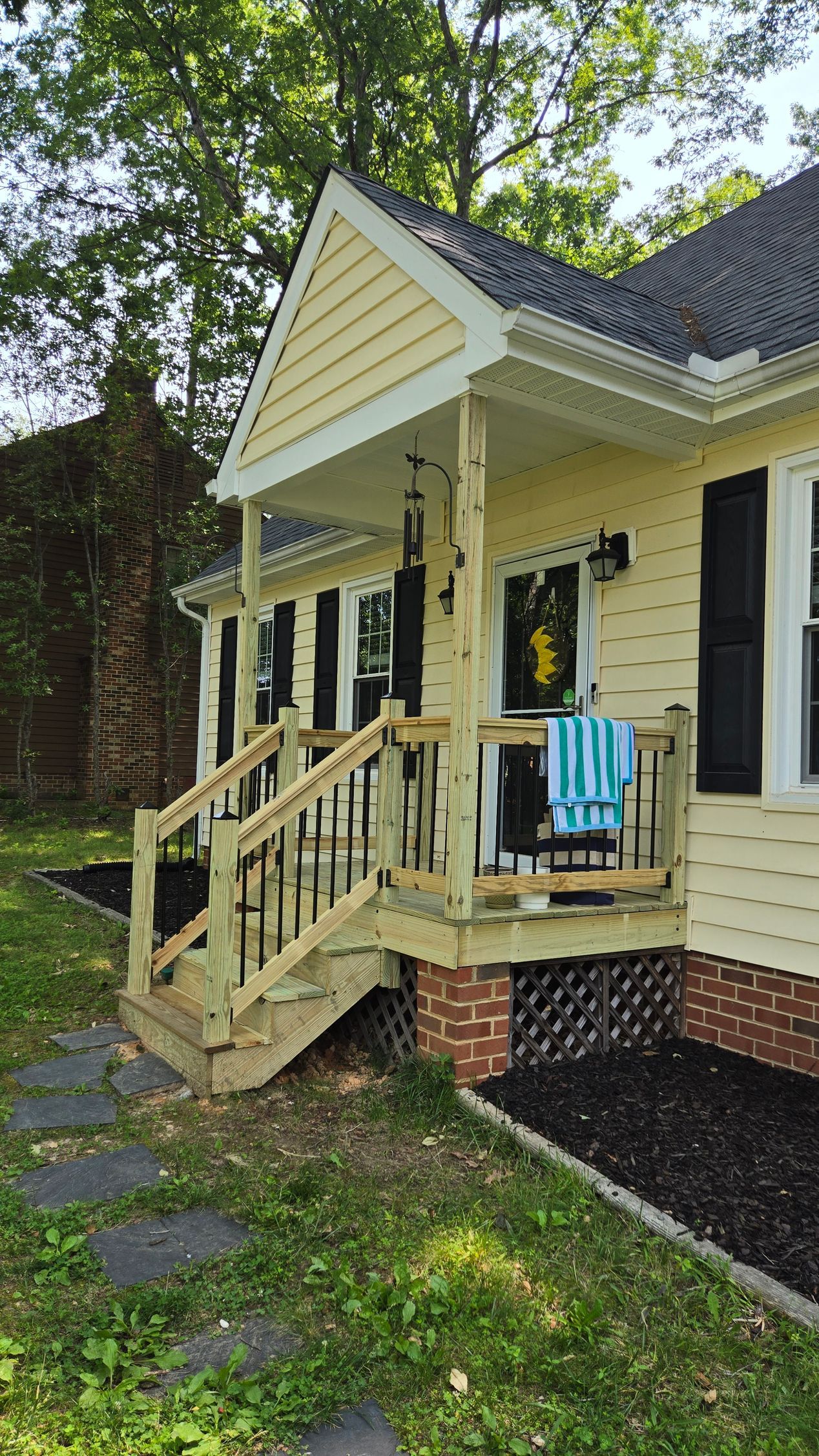 Yellow house porch with white trim, steps, and a blue chair beside the front entrance