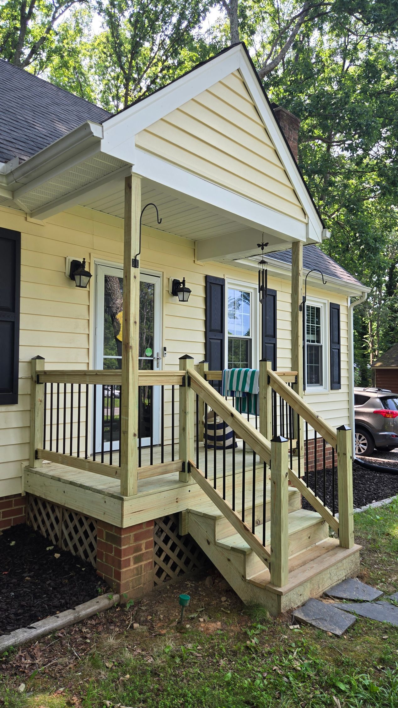 Small beige house porch with wooden steps, railings, and a ramp under a gabled roof.