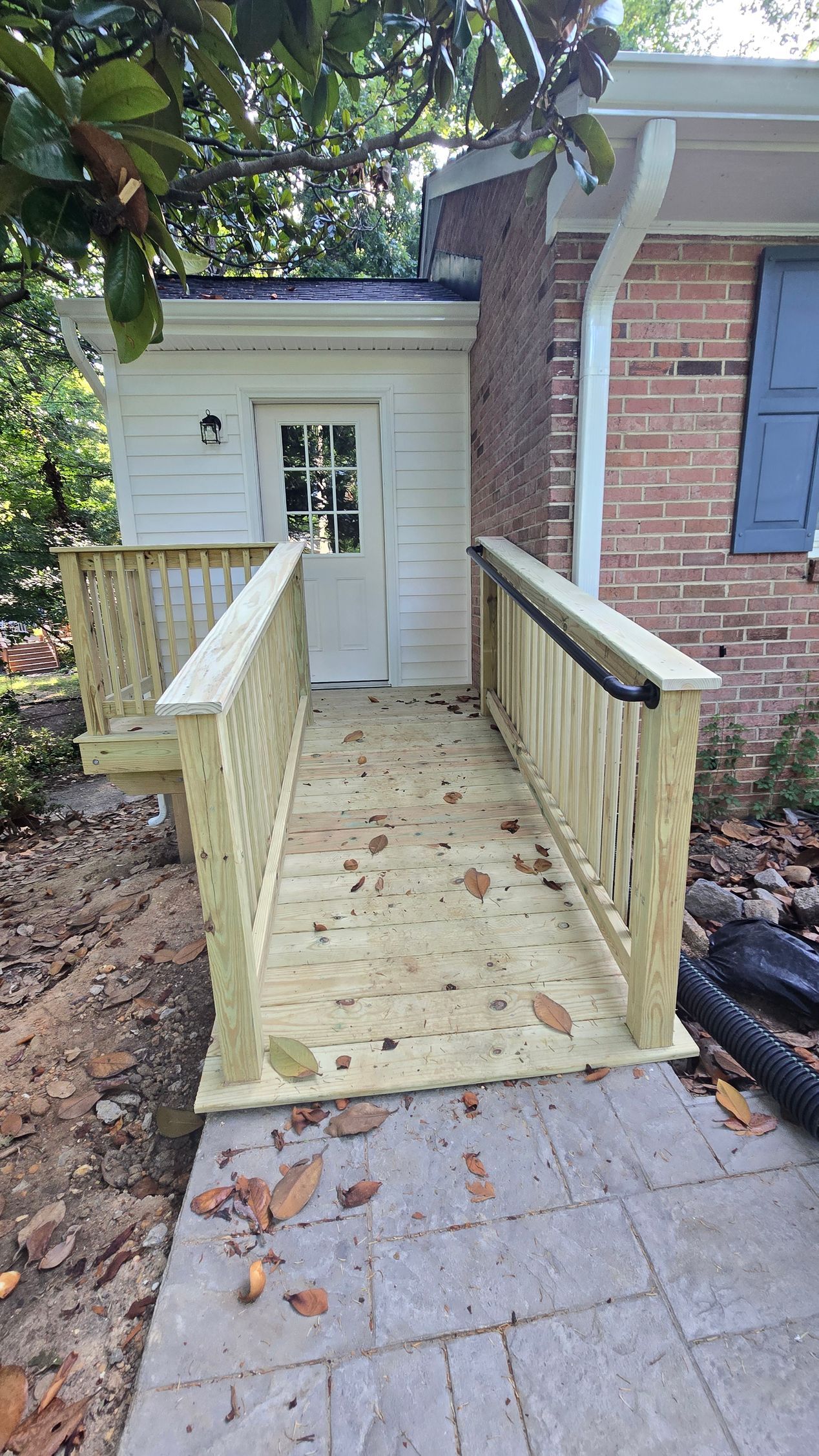 Wooden wheelchair ramp leading to a white door on a brick house exterior