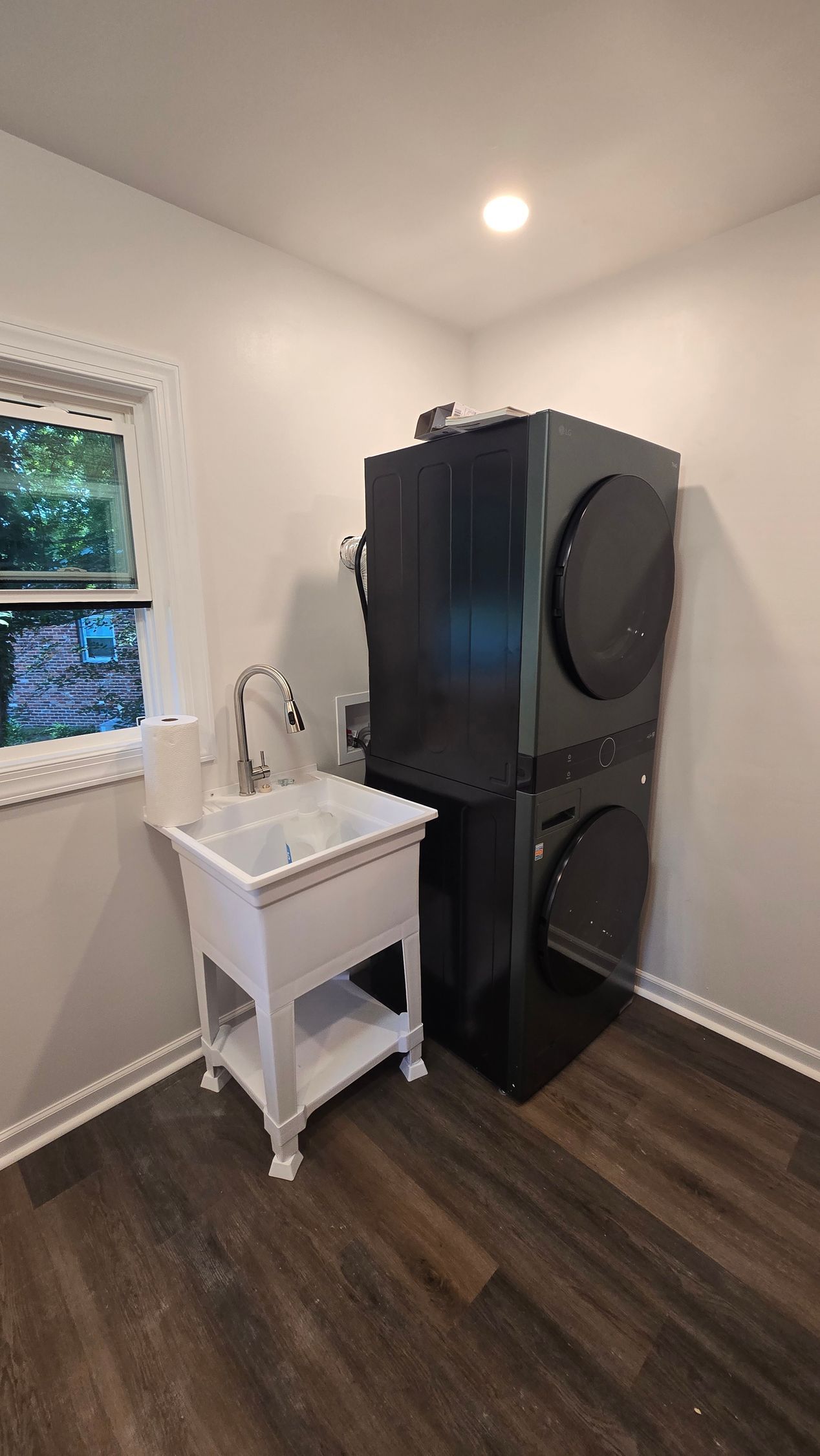 Laundry room with stacked black washer and dryer beside a small white utility sink.