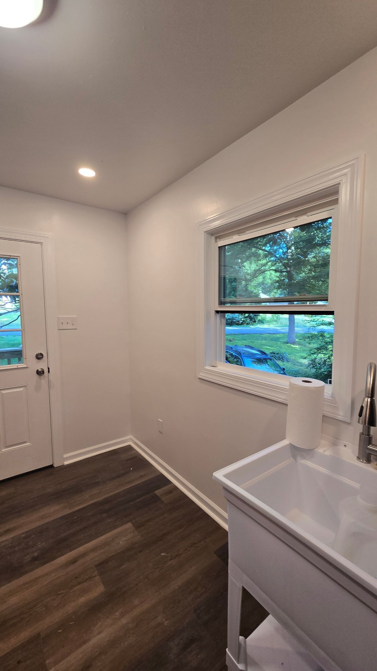 Small white room with dark wood floor, window, door, and white sink cabinet.