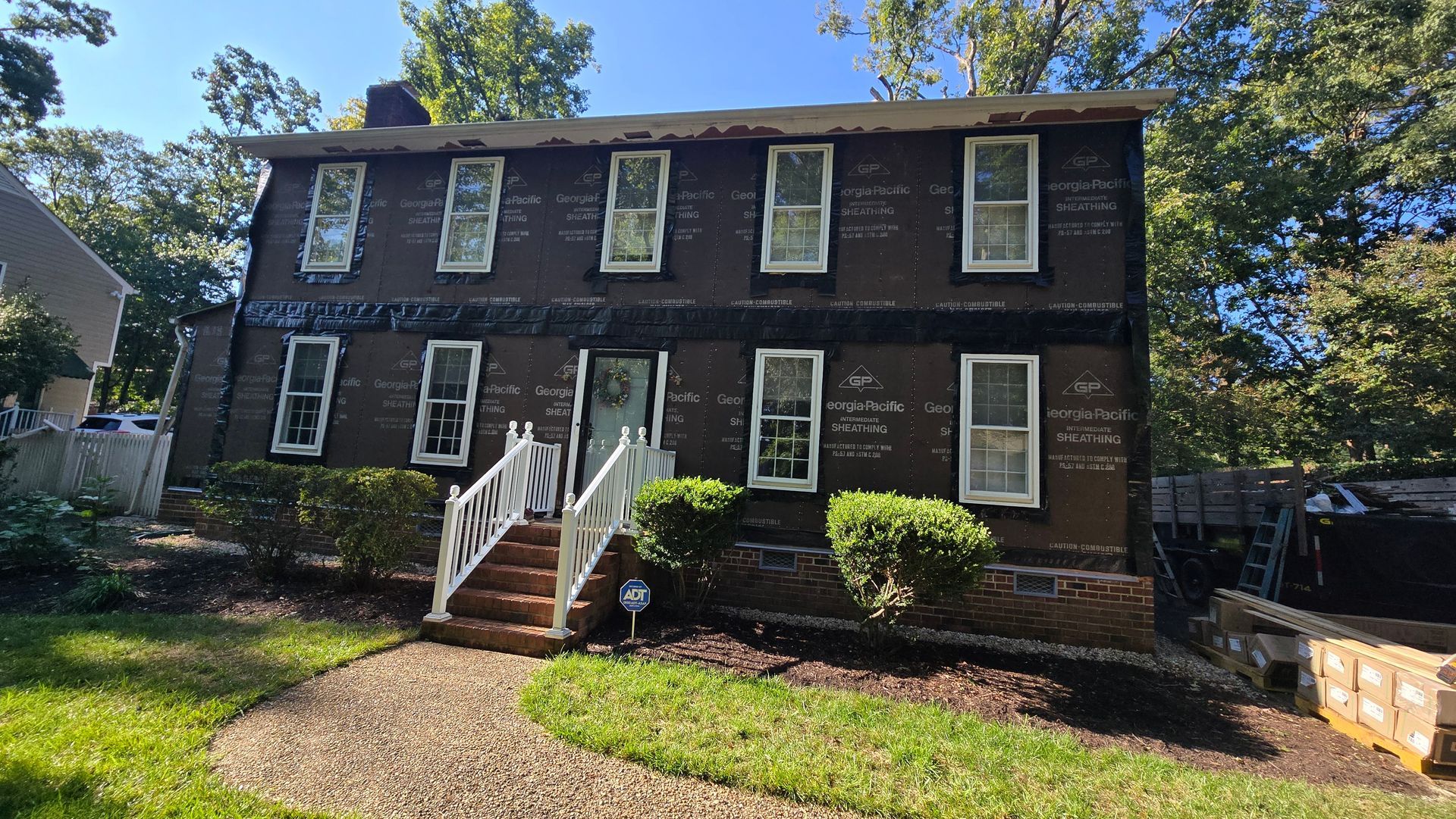 Two-story brick house with white trim, front steps, and shrubs in a sunny yard