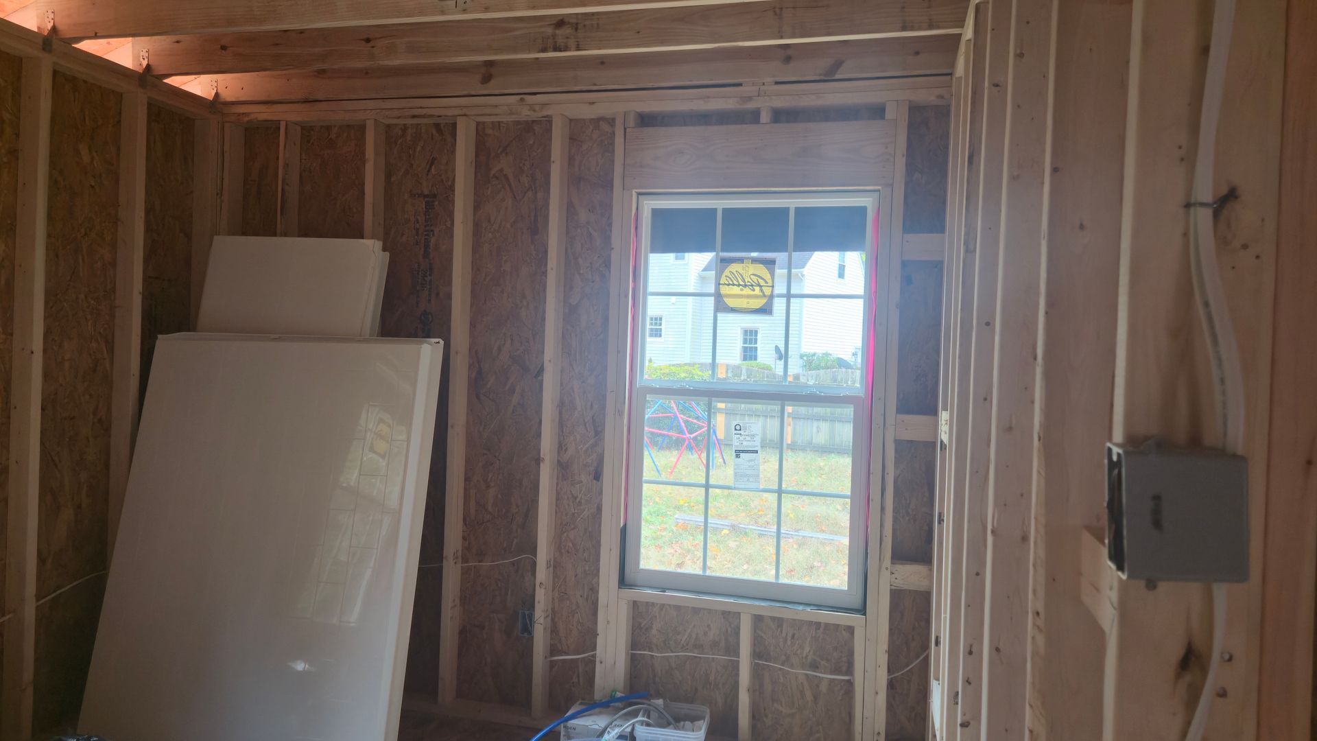 Unfinished room with exposed studs, a window, insulation, leaning boards, and an electrical box.