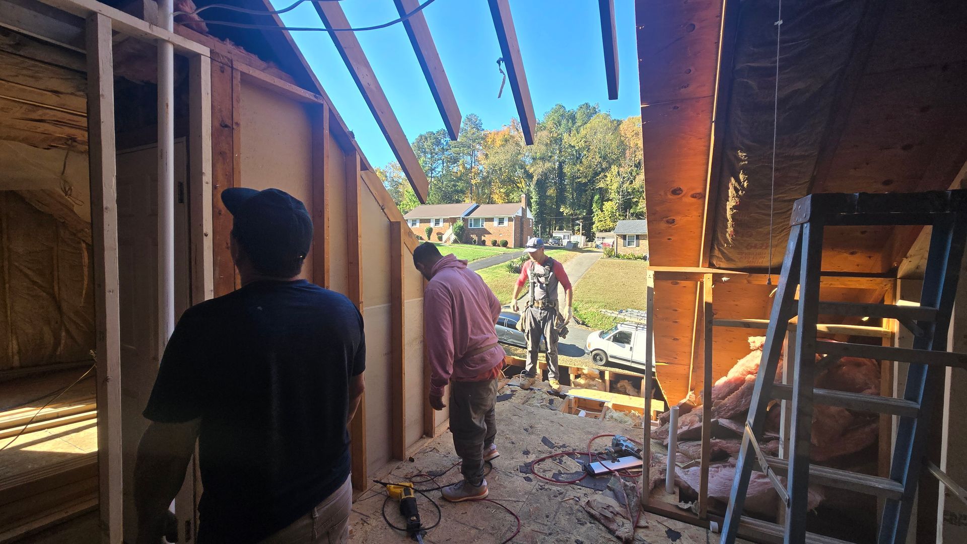 Workers in a narrow construction corridor with exposed wooden framing and blue sky overhead