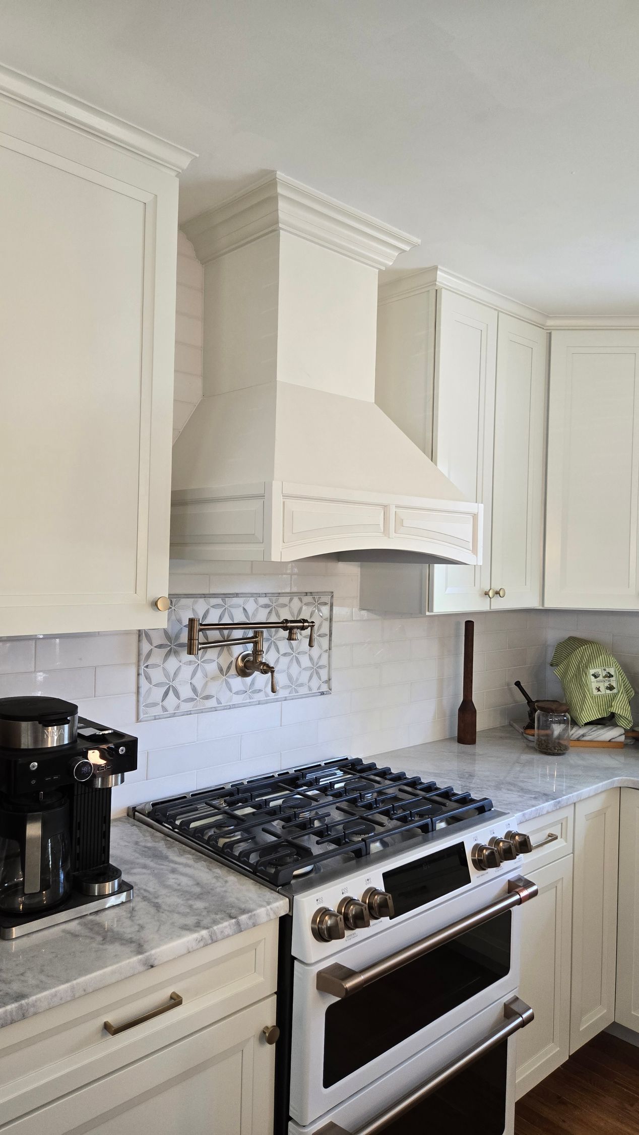 Bright white kitchen with gas range, hood, and cabinets, featuring a coffee maker on the counter.