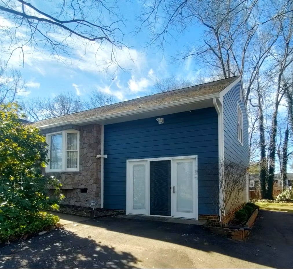 Blue house exterior with white double doors, brick side wall, and bare trees in a driveway.